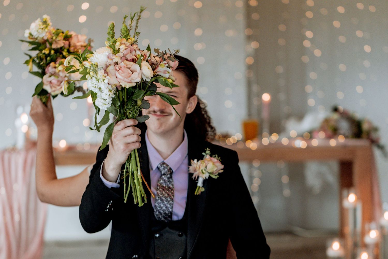 Wedding party stands outdoors holding bouquets of white and pink flowers against a twinkle light backdrop.