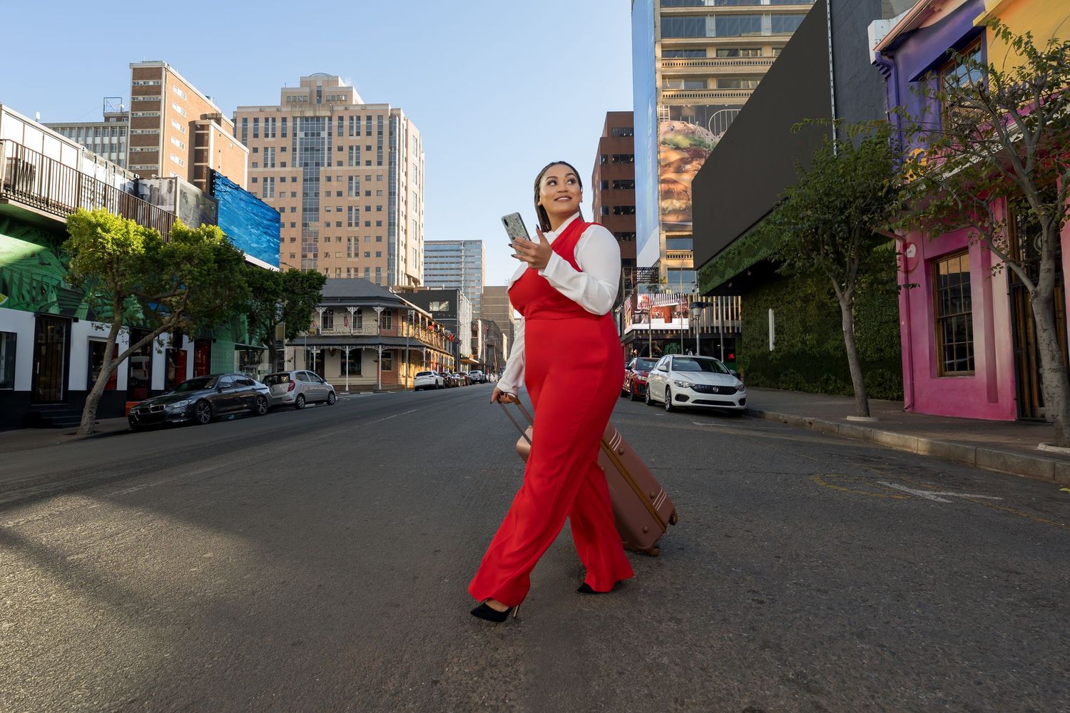 A person in a vibrant red jumpsuit strikes a pose on an urban street with tall buildings in the background.