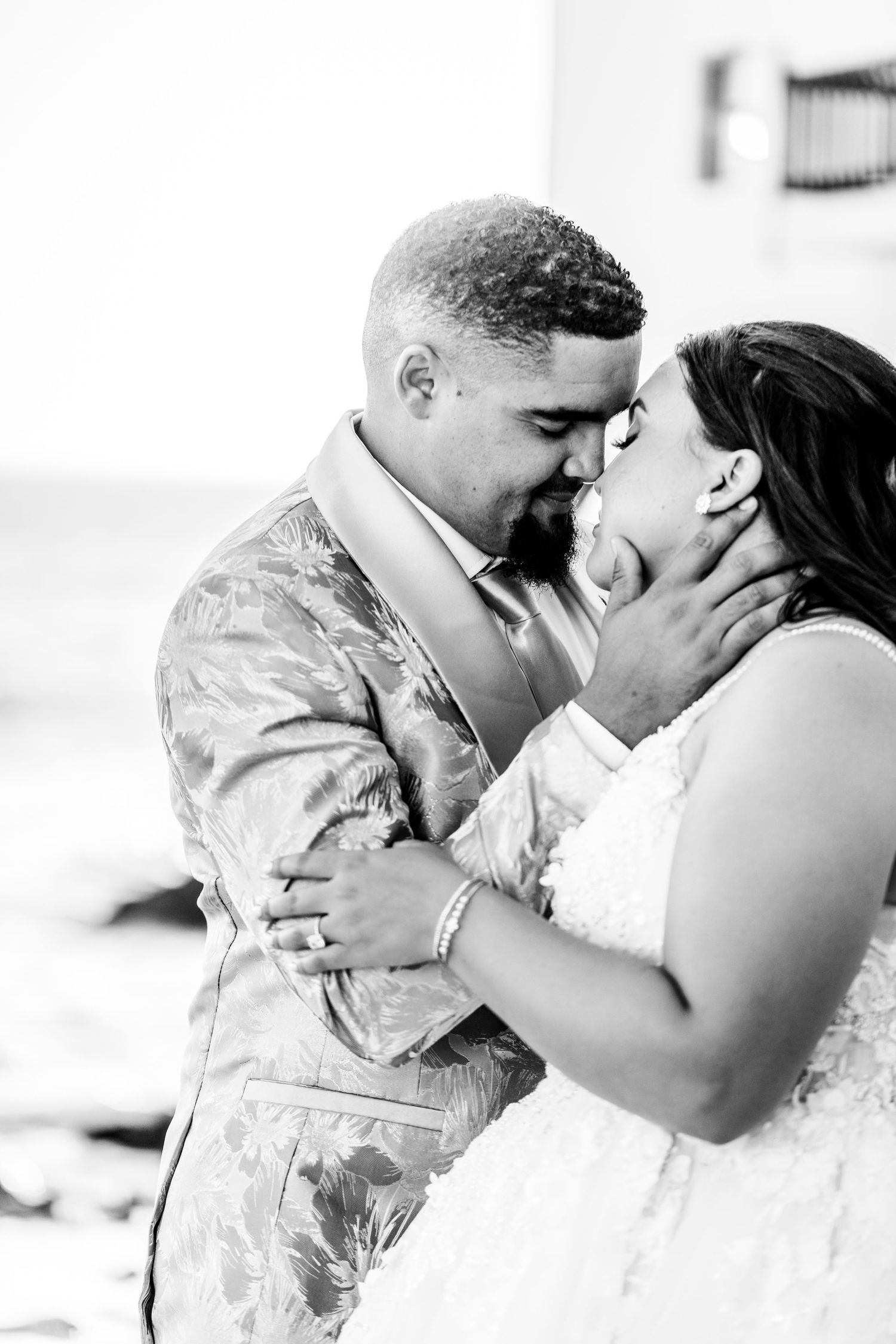A romantic black and white wedding photo of a couple sharing an intimate moment in formal attire.