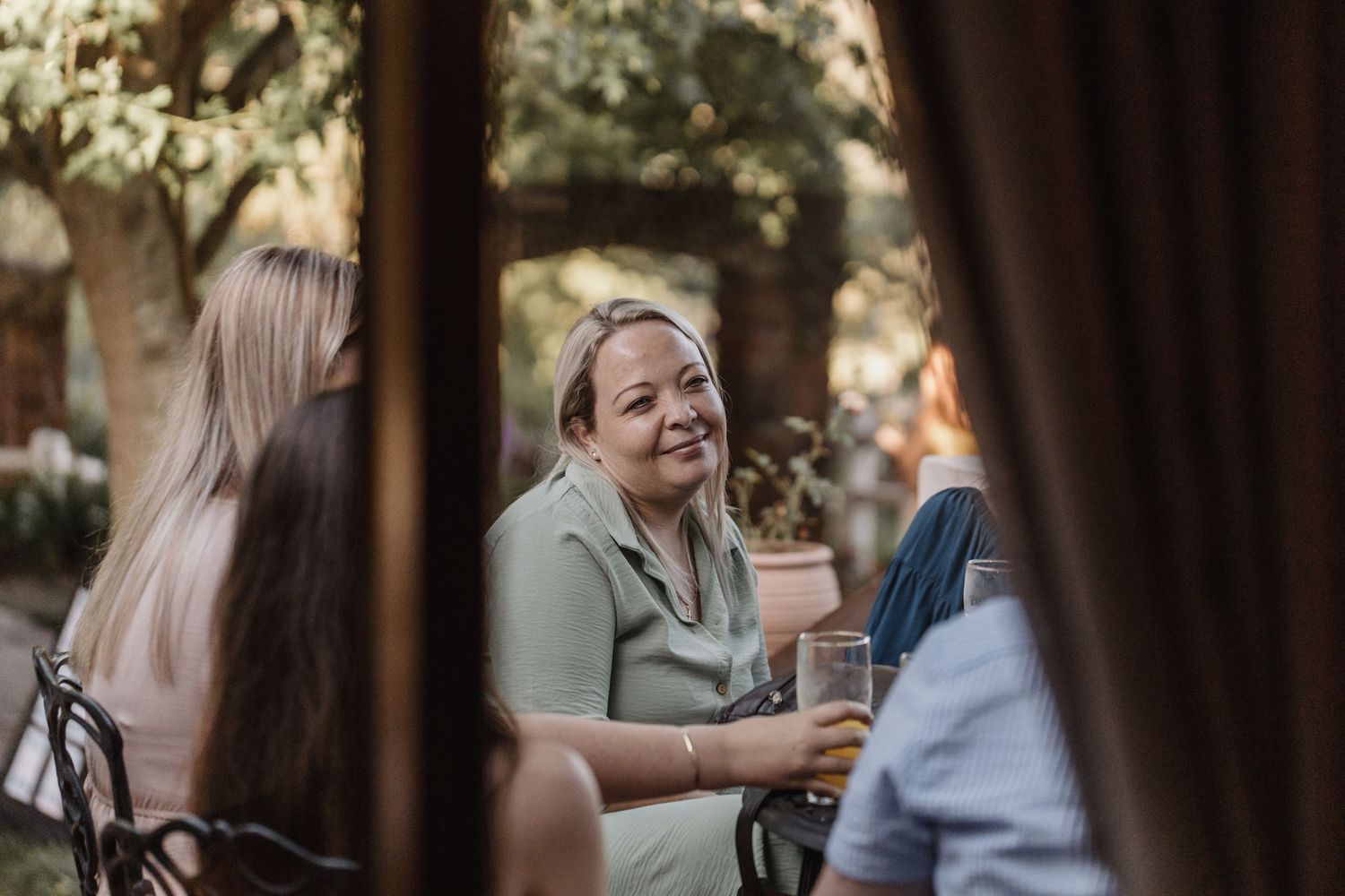 Three people engaging in casual conversation outdoors while holding coffee cups and smiling.