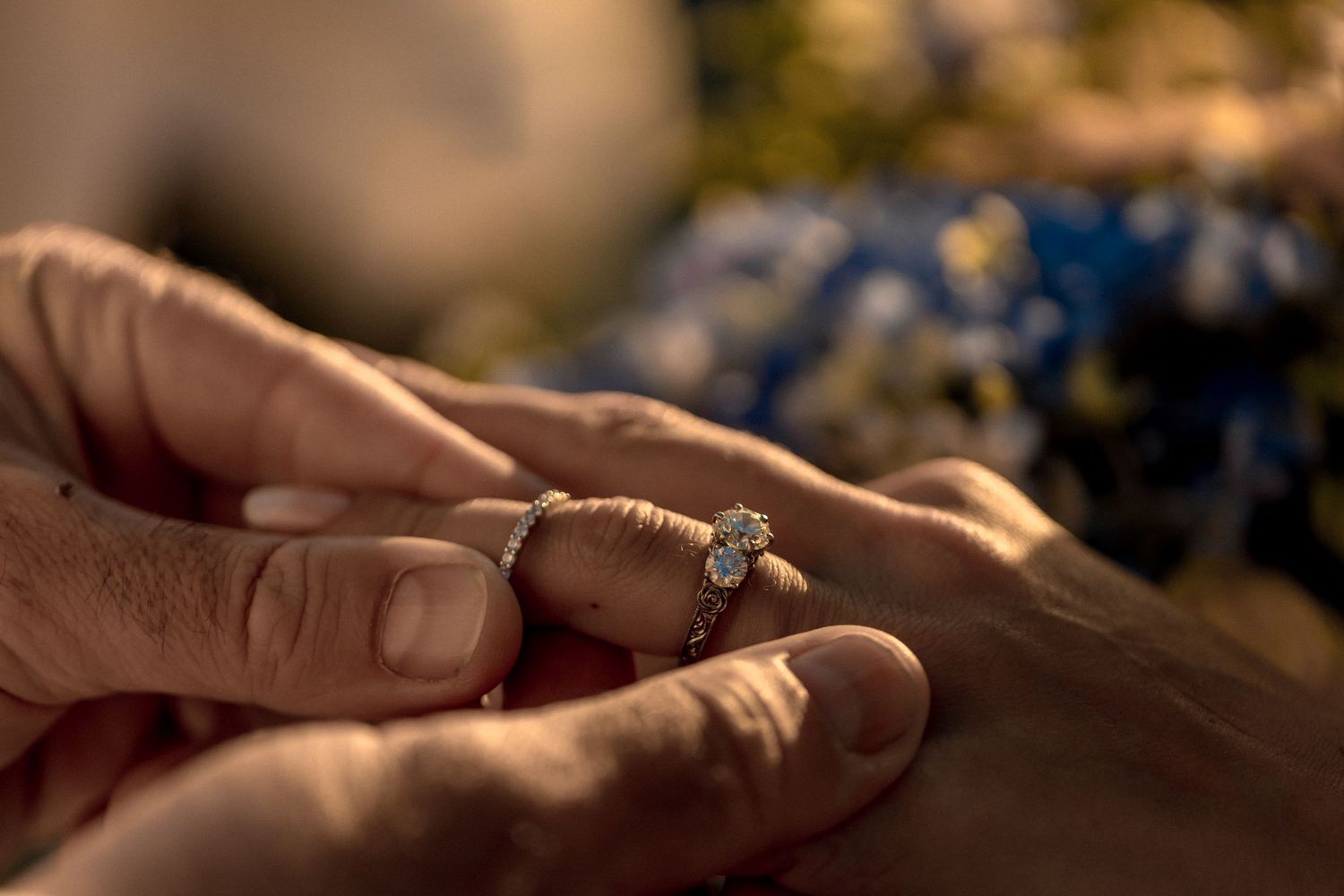 Close-up view of hands exchanging engagement ring in outdoor setting with soft bokeh lighting.