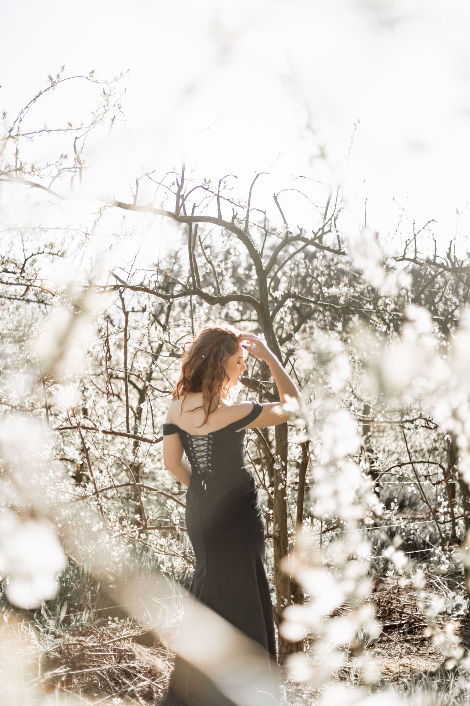 Ethereal winter scene captures a black-dressed figure through delicate white blossoms in soft natural lighting.