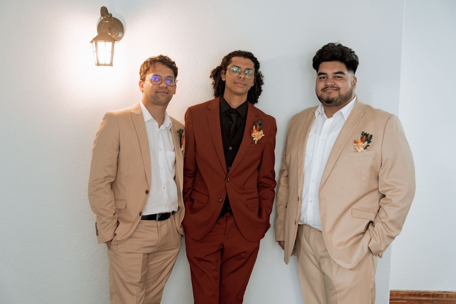 A dapper group of people wearing beige blazers and brown suits pose together against a white backdrop.
