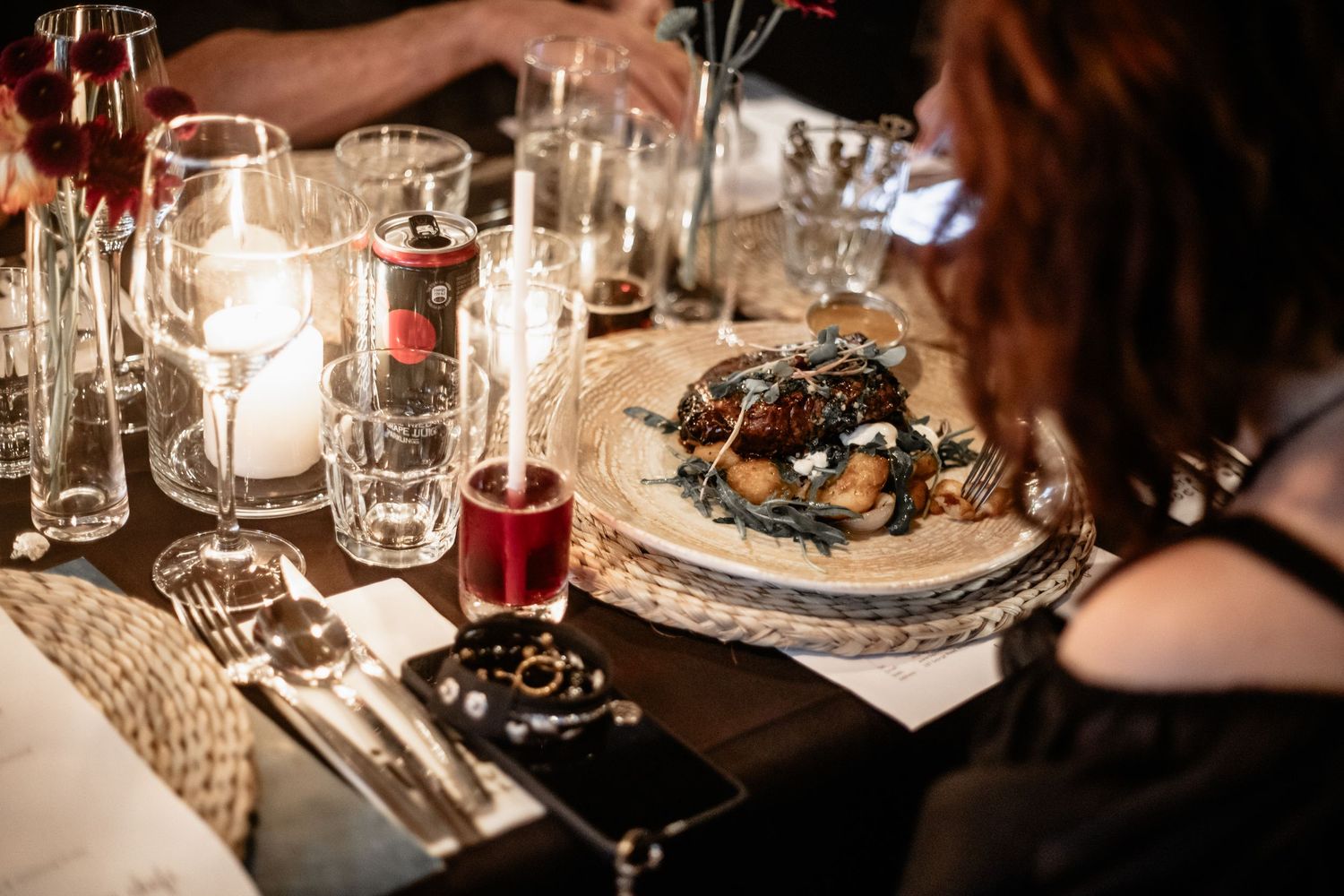 An intimate dinner setting with glowing candles, wine glasses, and a gourmet plate of food on a rustic table.