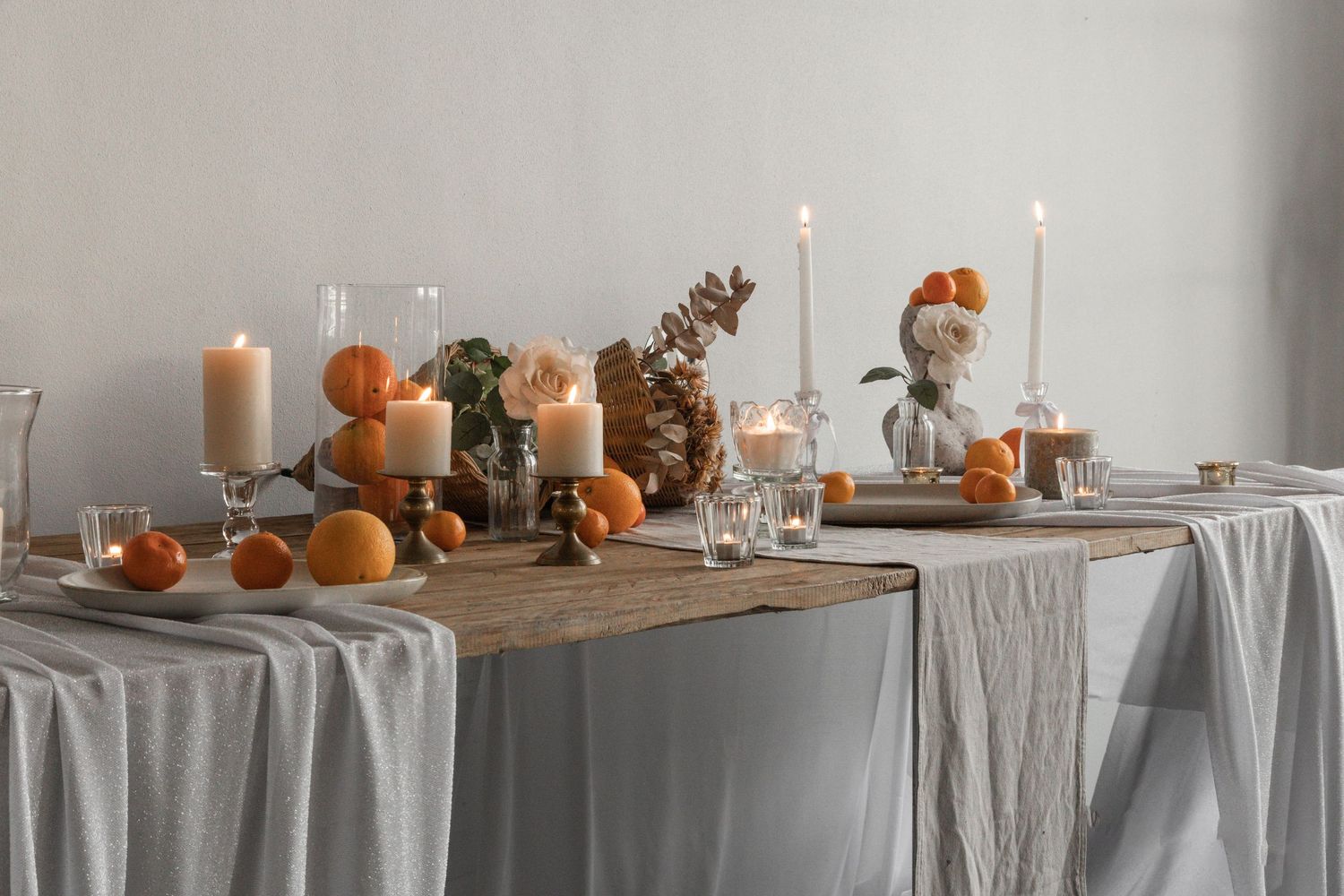 Elegant tablescape with white linens, pumpkins, and candleholders arranged in a long banquet style setting.