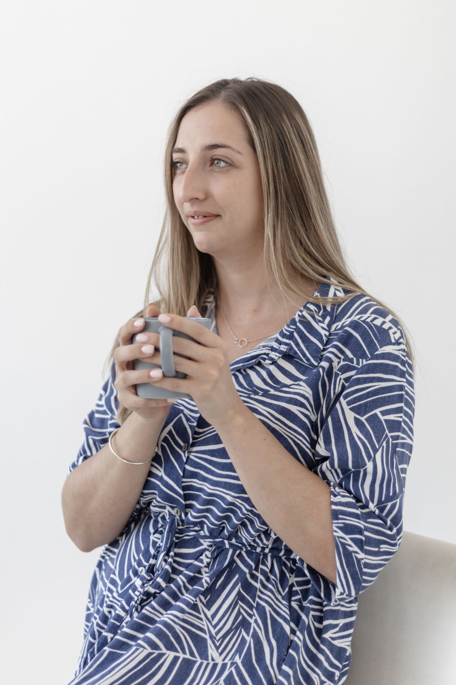 Woman in blue and white striped blouse sitting and holding phone while looking thoughtfully to the side.