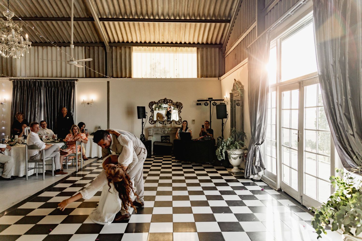 A panoramic view of a dance studio with black and white checkered floors and large windows letting in natural light.