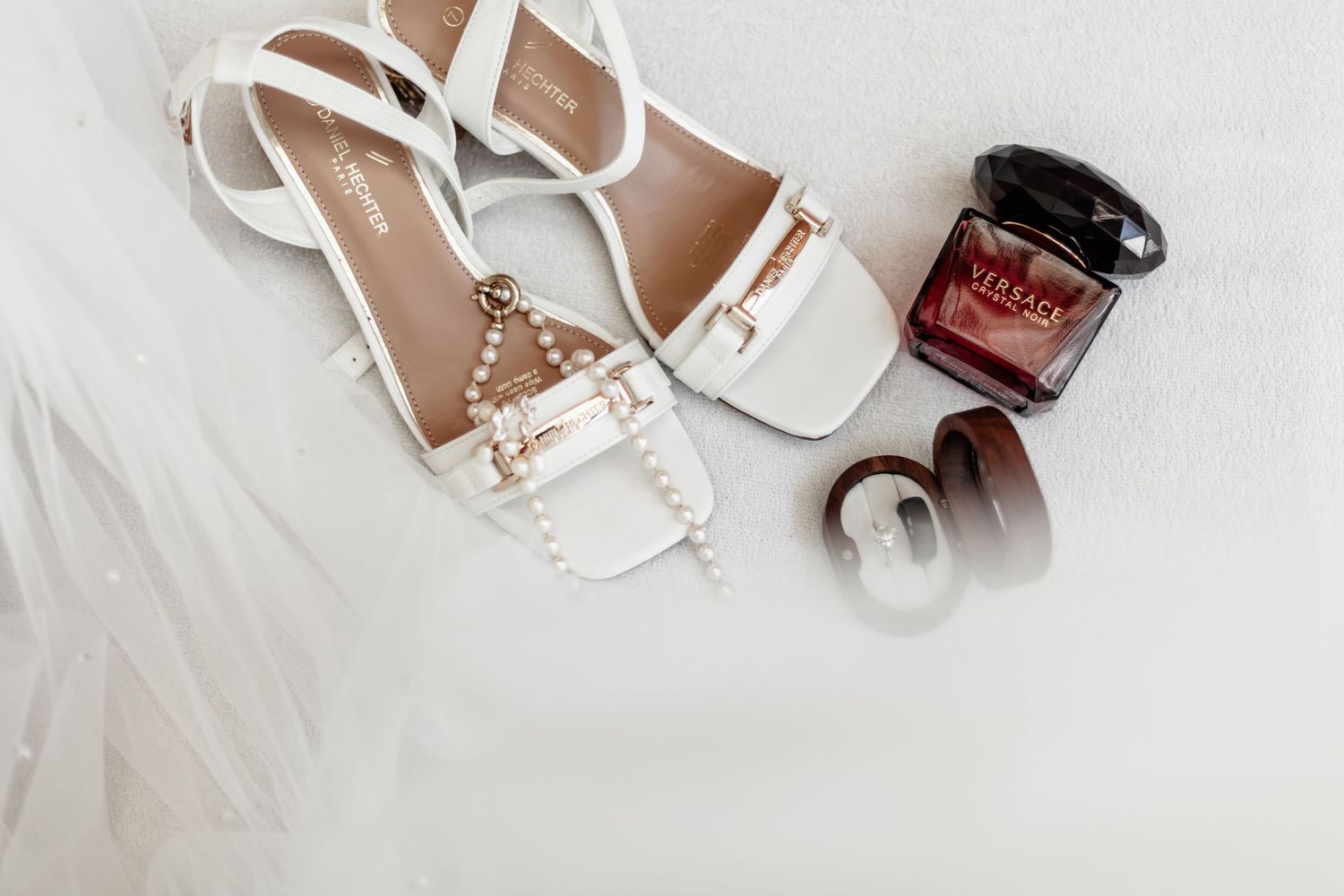 White leather strappy sandals with gold buckle details arranged on a light gray background with nail polish bottle.