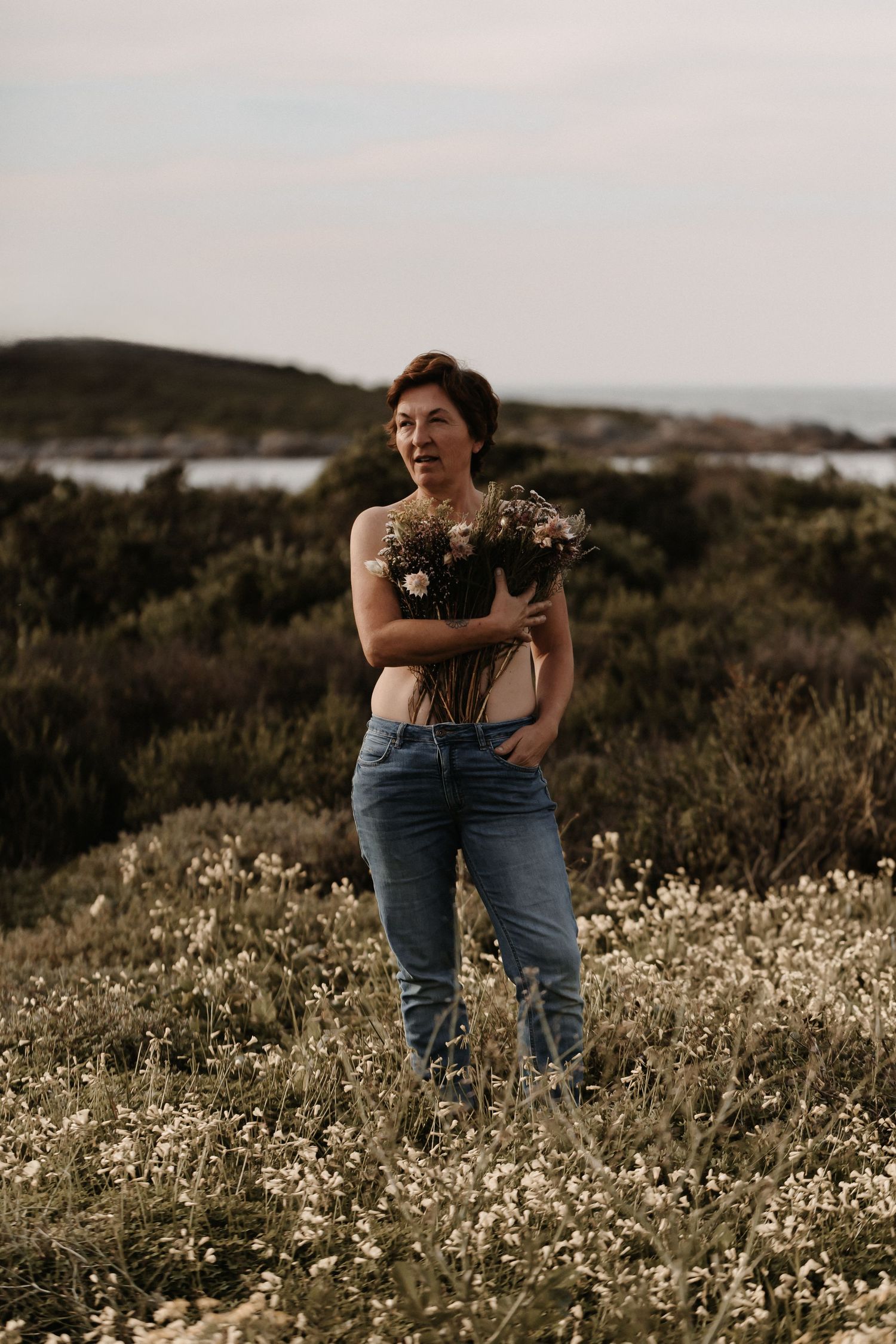 Someone stands in a field of white wildflowers at sunset with mountains visible in the distance.