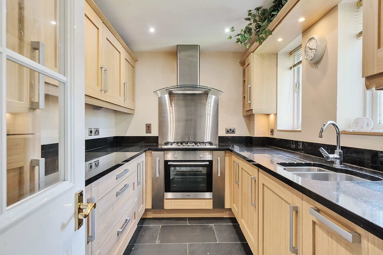 Modern galley kitchen with cream cabinets, black granite countertops and stainless steel appliances.