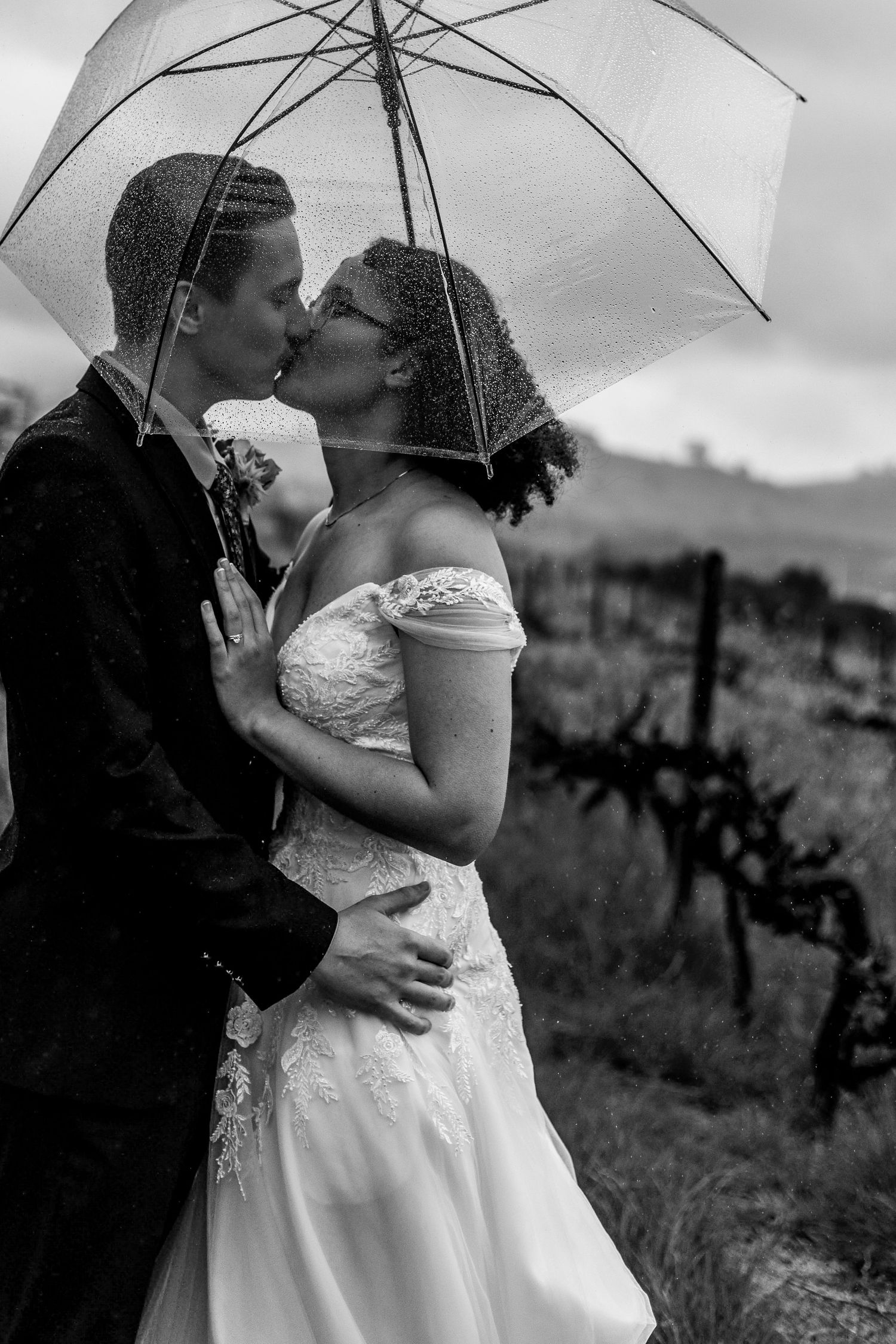 A romantic black and white wedding photo series showing a couple embracing under umbrellas in a picturesque outdoor setting.
