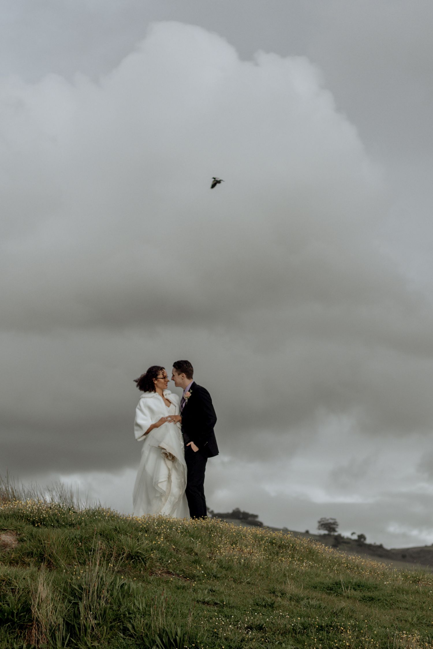 Newlyweds embrace on a hilltop under dramatic stormy skies in a series of romantic wedding photographs.