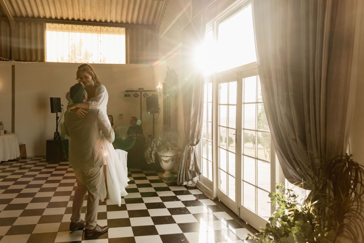 Couple embracing in golden sunlight on checkered dance floor during romantic wedding reception.