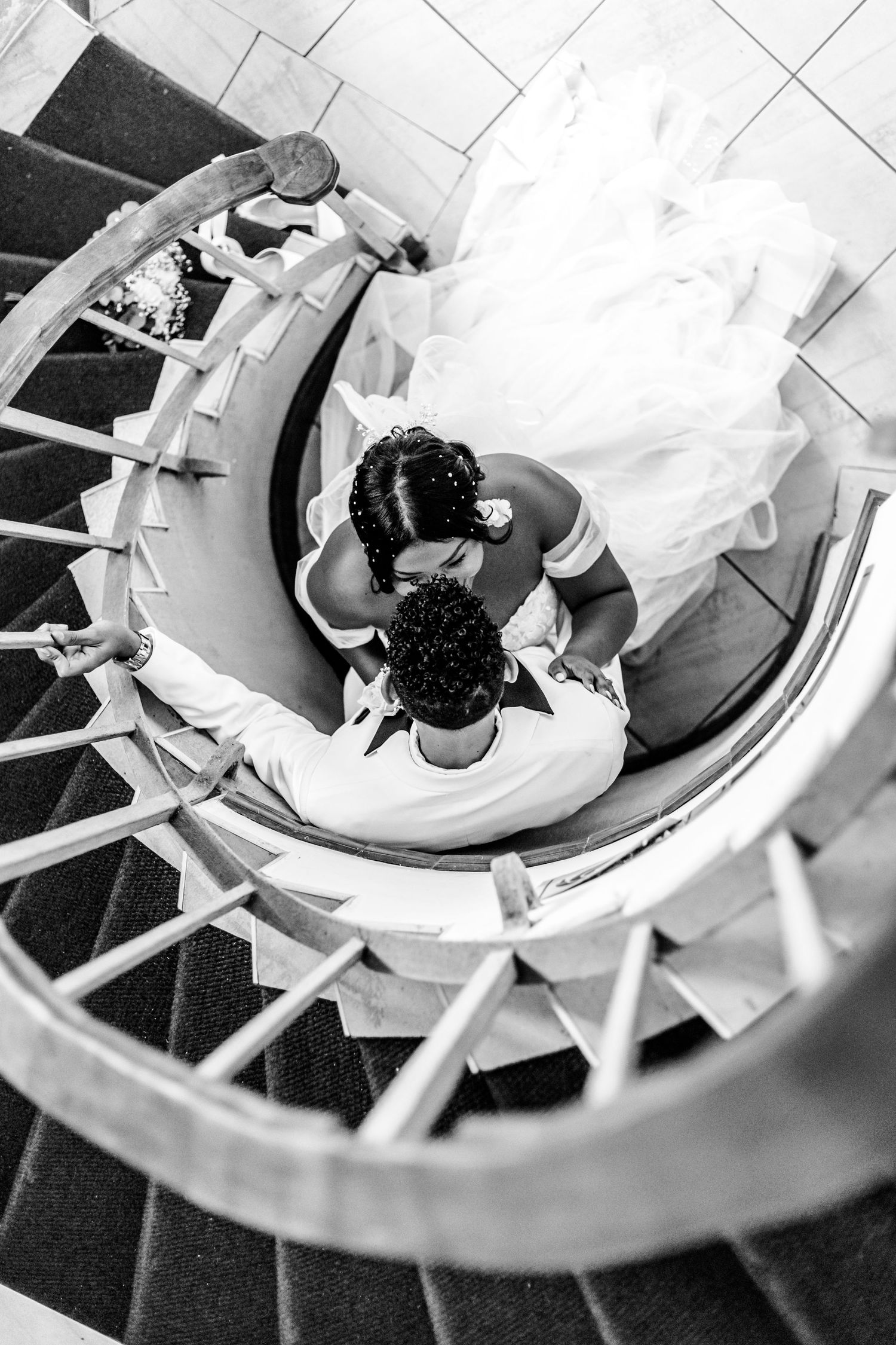 Aerial view of two people in formal attire descending a spiral staircase with white tile and black accents.