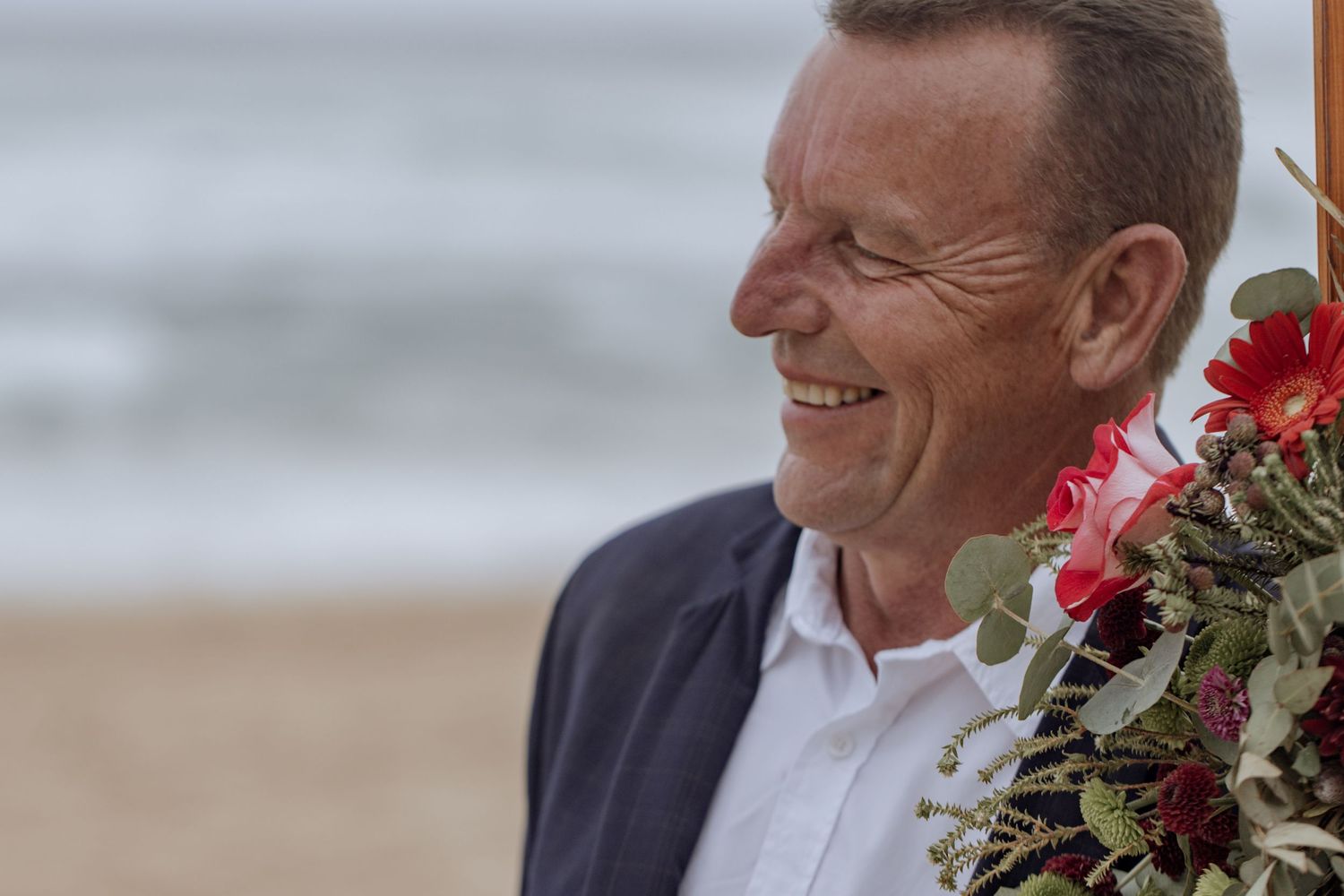 A side view portrait shows someone smiling while standing on a beach with red flowers visible to the side.