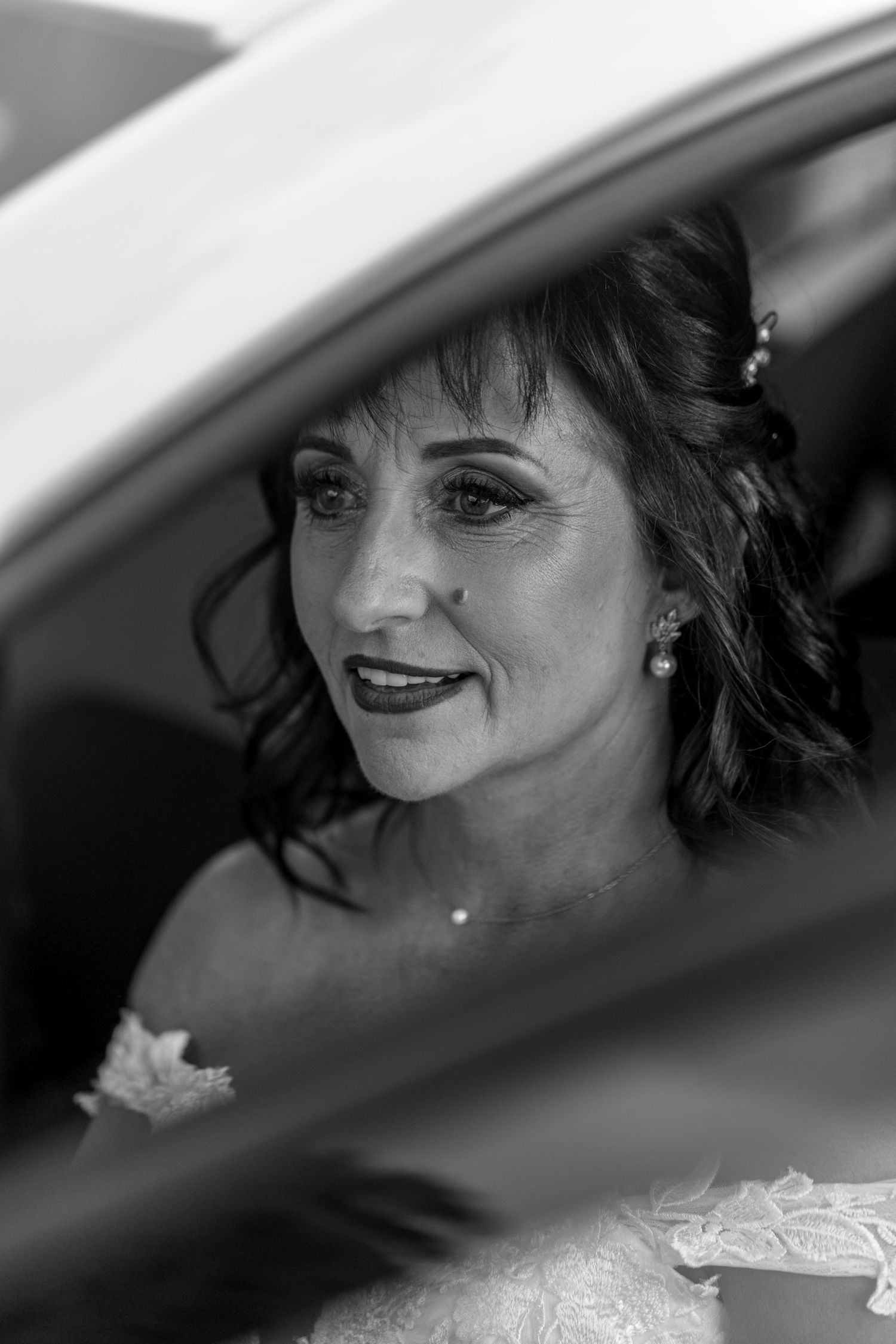 Black and white portrait through a car window shows a joyful smile and glowing expression.