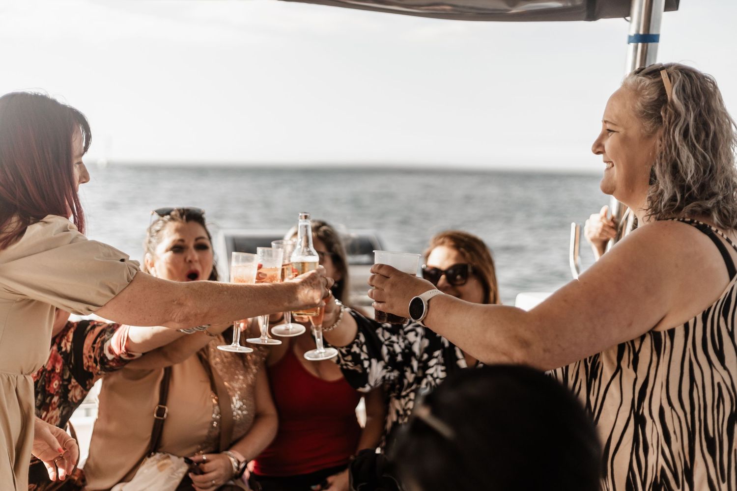 A group of friends making a celebratory toast with drinks while enjoying a boat ride on the ocean.