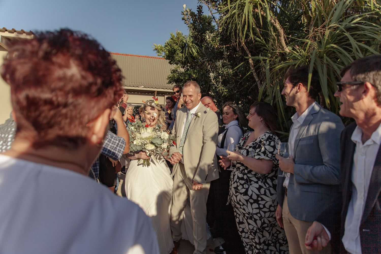 Wedding guests gather for an outdoor celebration under palm trees at a daytime reception.