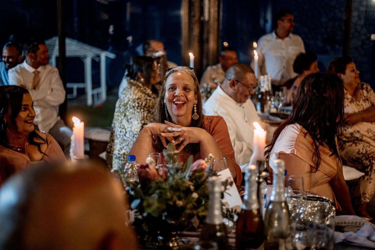 Guests laughing and enjoying themselves at an evening candlelit dinner party with floral centerpieces.