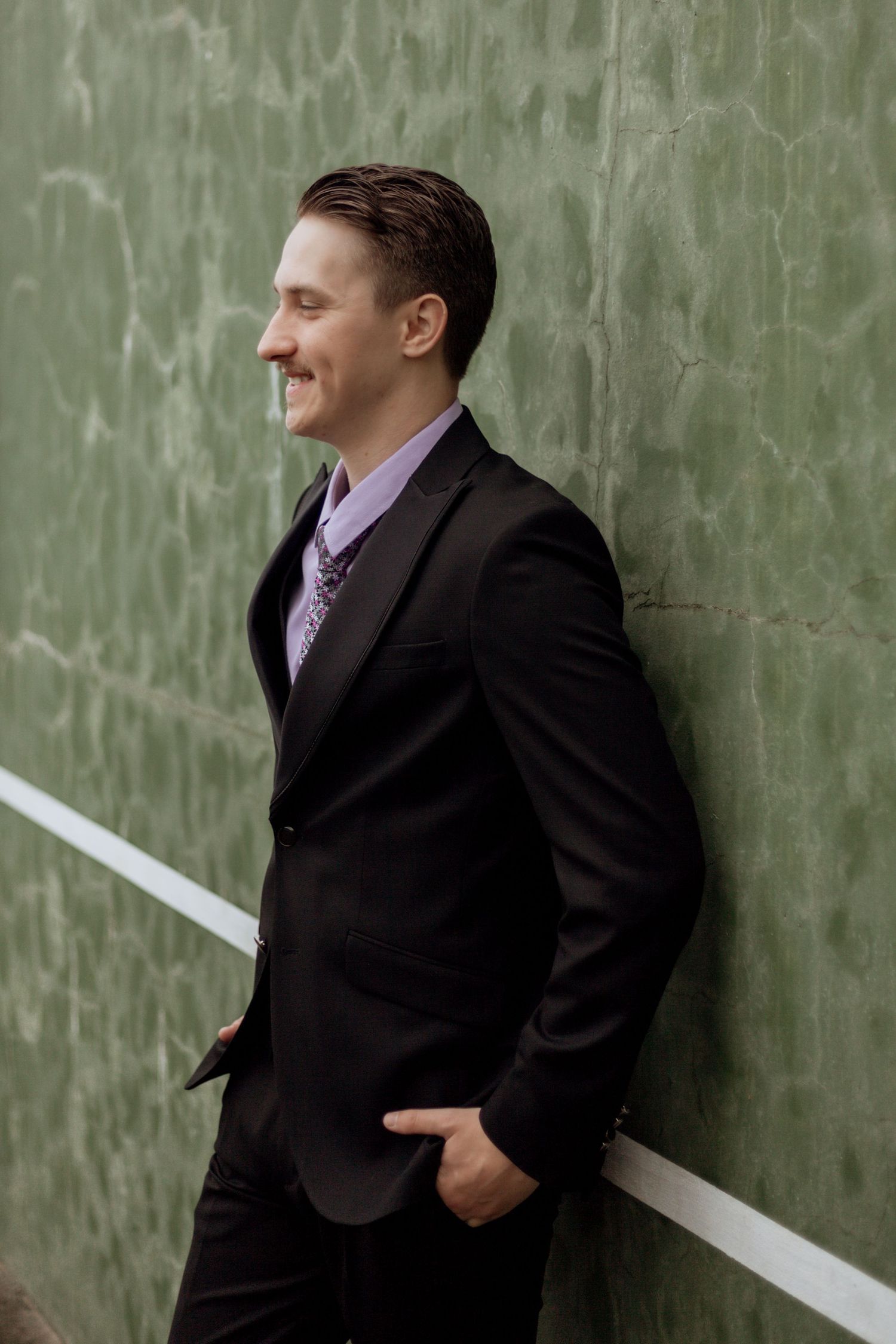 Professional in black suit laughs joyfully against green textured wall with white diagonal line.