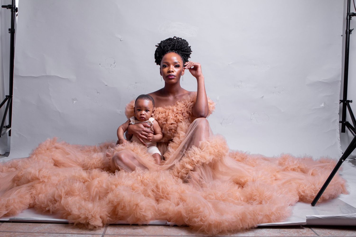 Mother and baby in matching peach tulle gowns pose during studio photoshoot against light grey backdrop.