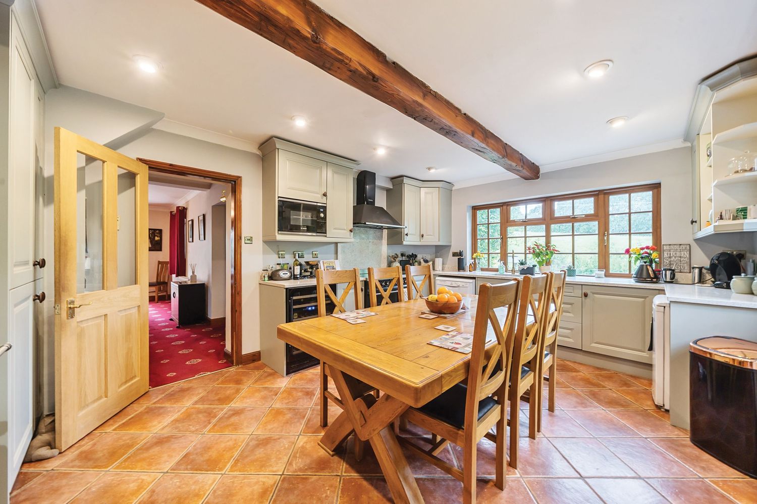Bright country kitchen with exposed wooden beams, terracotta floors, and a wooden dining table in an open concept space.