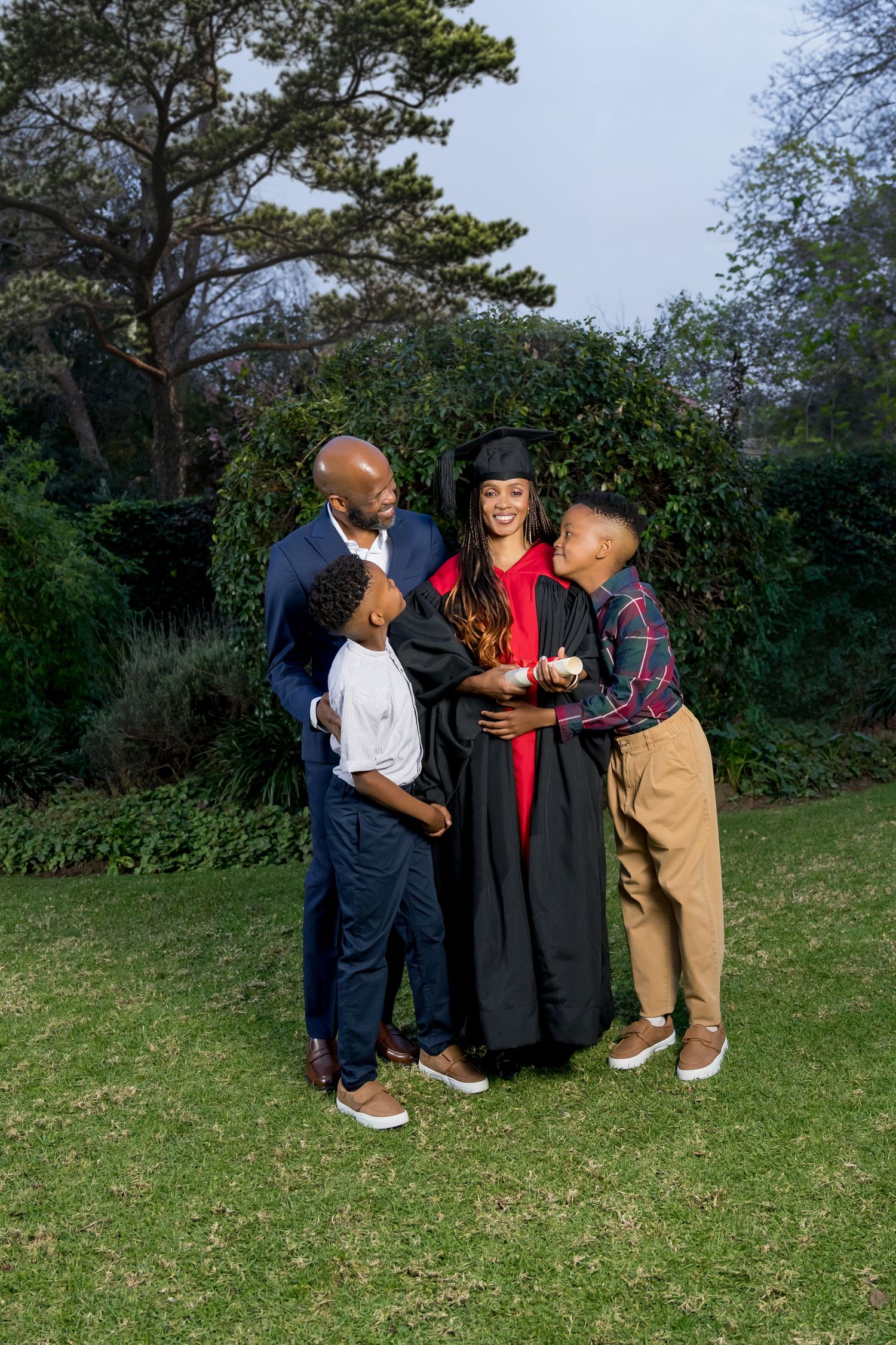 A graduation photo session outdoors with family members in formal attire on a grassy lawn with trees in the background.