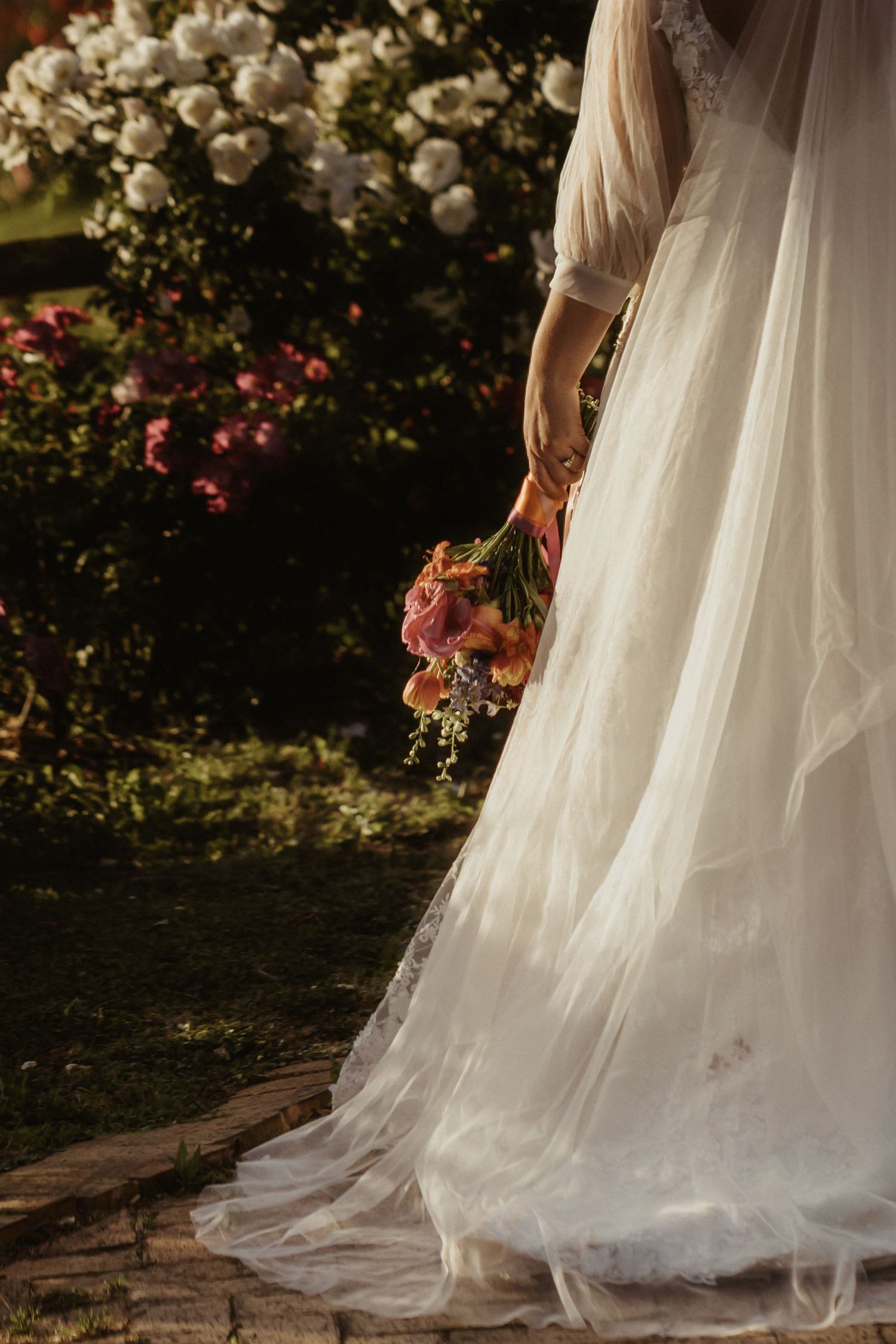 White wedding dress flowing in a garden setting with blooming roses and delicate details.