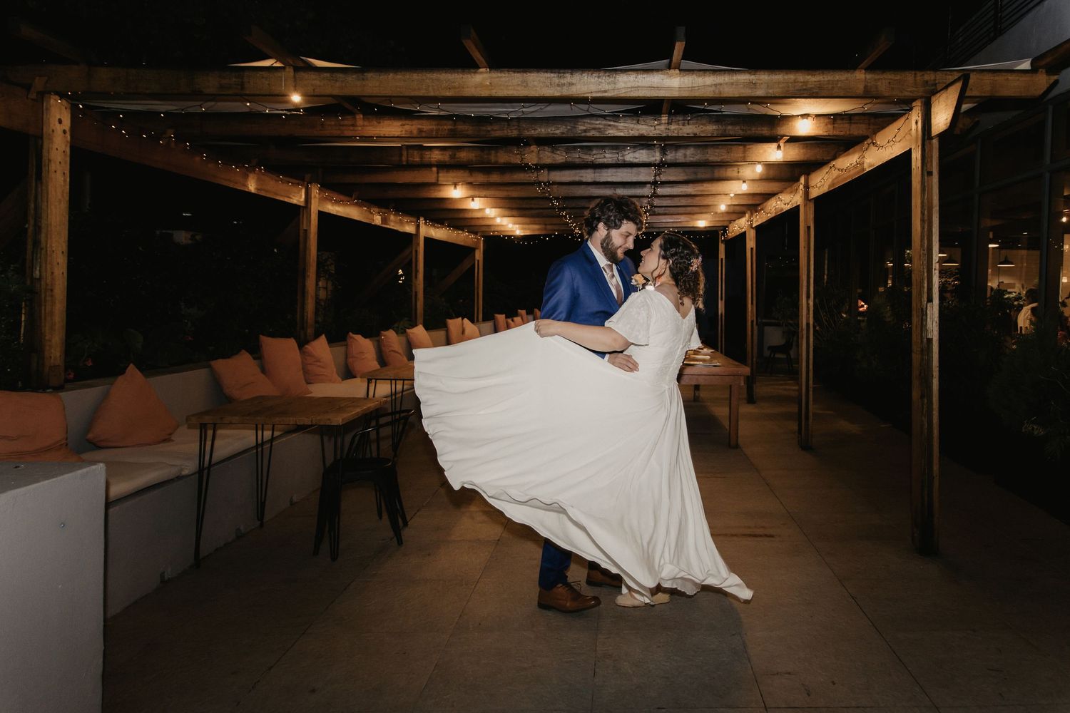 A couple dances intimately in a rustic venue with wooden beams and soft lighting overhead.