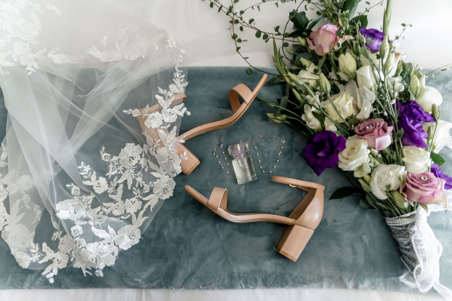 Wedding accessories including bouquet, shoes, jewelry and decor arranged artistically on gray background.