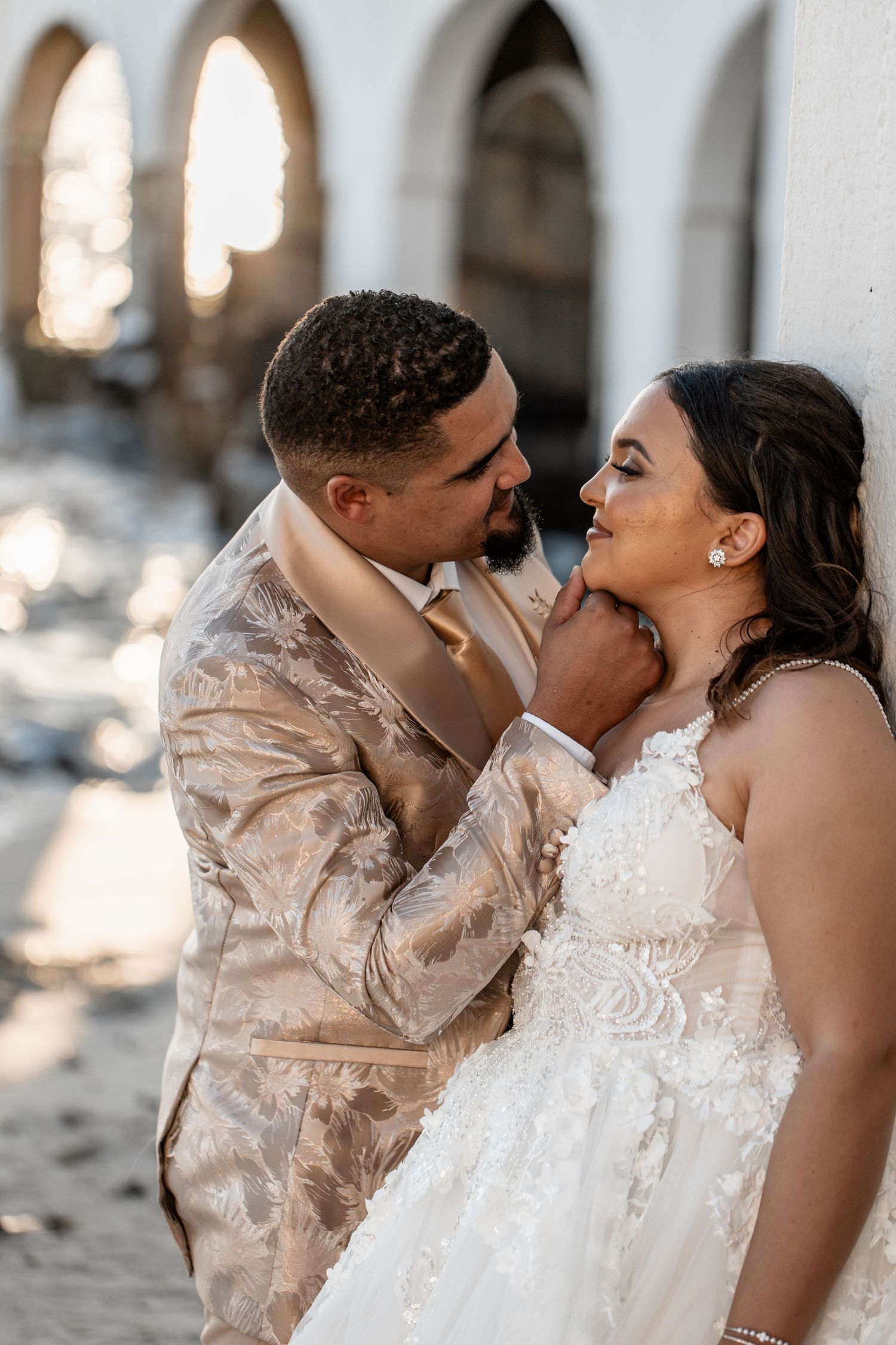 Romantic military couple sharing an intimate moment at an archway in elegant wedding attire.