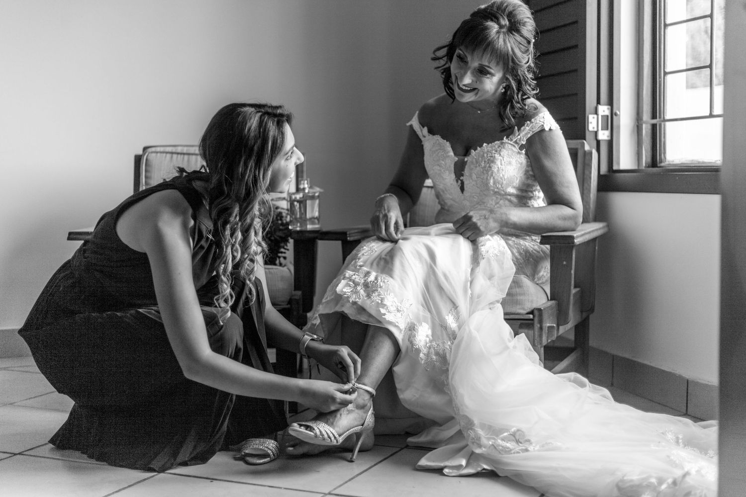 Black and white photo showing final preparations and adjustments to a wedding dress in an intimate indoor setting.