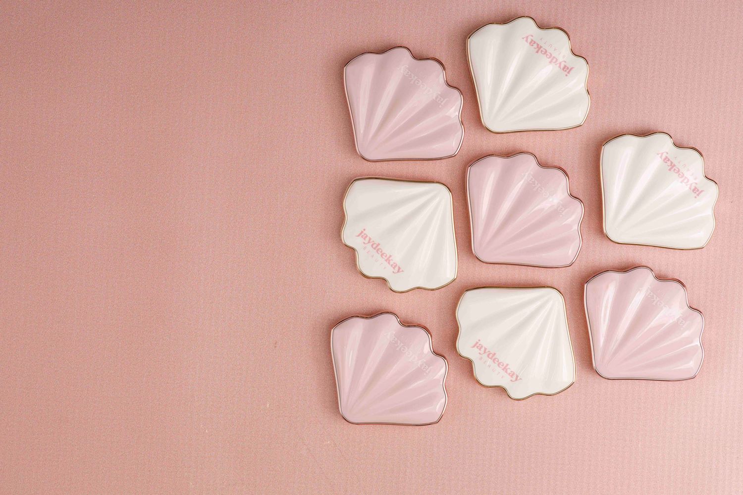 White meringue cookies arranged in rows on a soft pink background create a minimalist pastel composition.