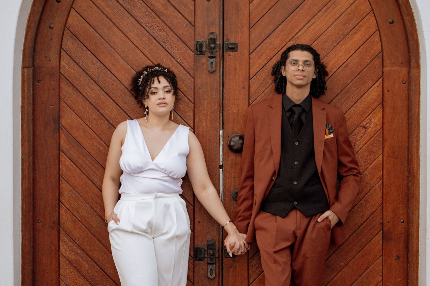 Three people pose in white and brown outfits in front of a wooden barn door.