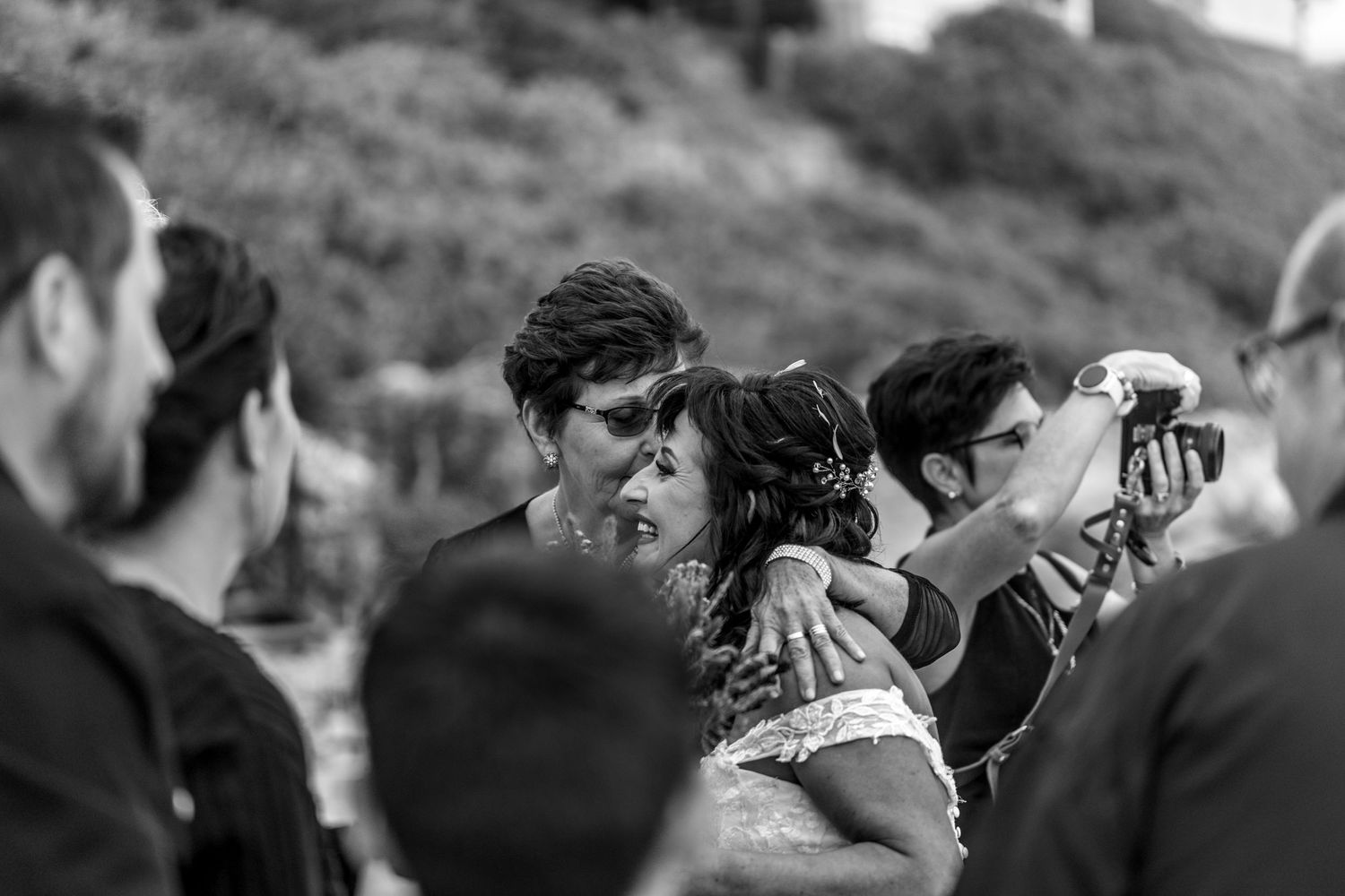A black and white candid shot shows photographers with vintage cameras gathered outdoors on a hillside.