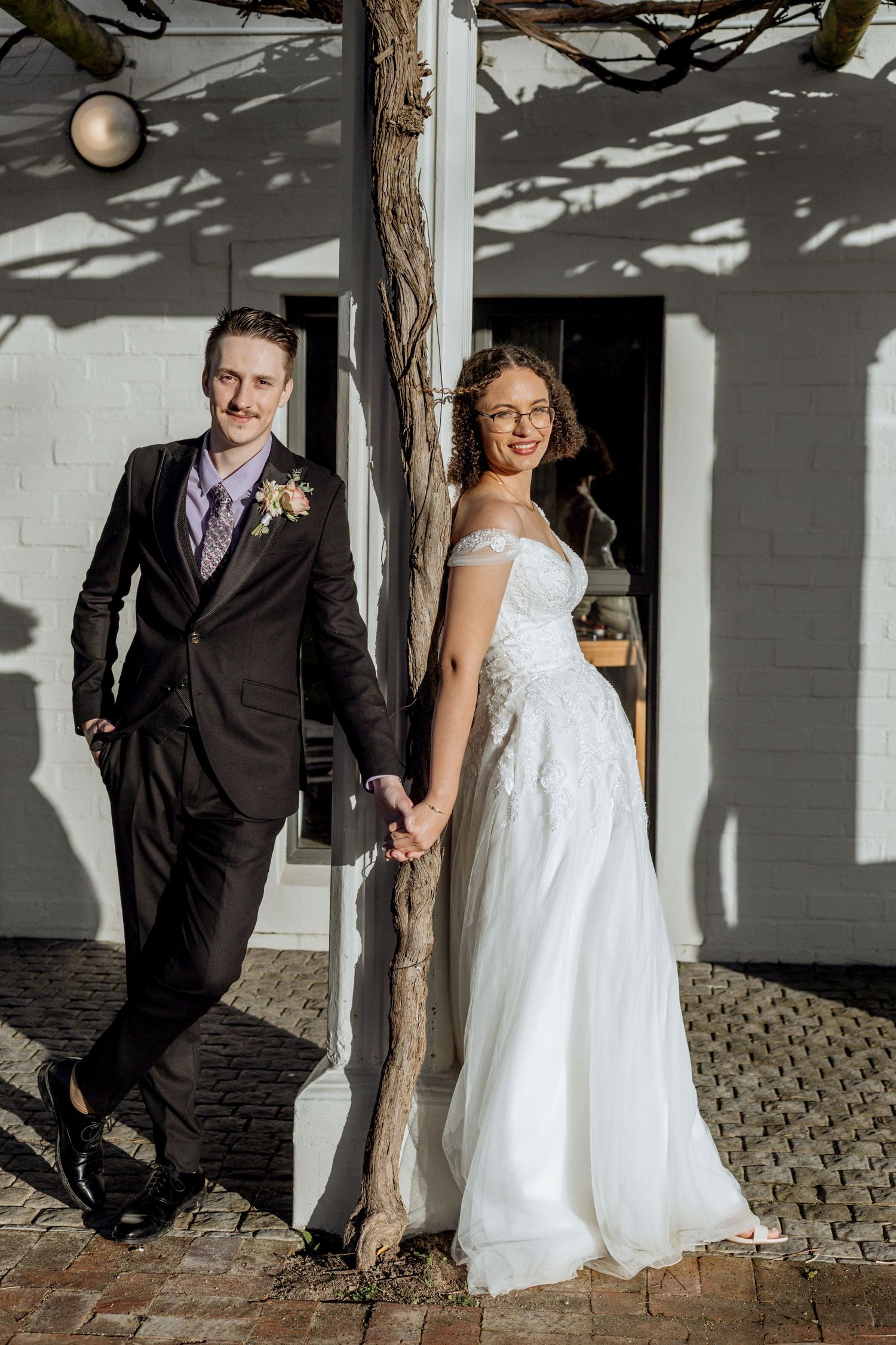A wedding couple poses in front of a white brick wall with dramatic shadows creating an artistic portrait series.