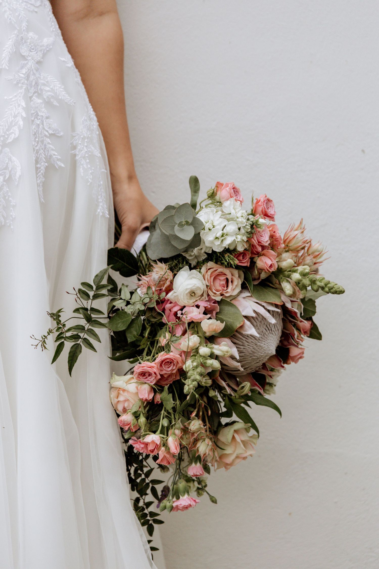 A pink and white floral bouquet with eucalyptus leaves being held against a white background.