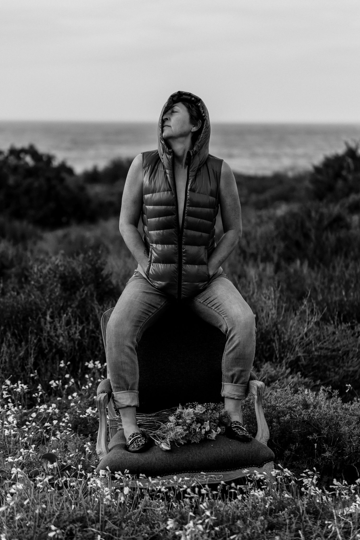 A series of artistic black and white photographs showing someone sitting in nature among wildflowers near the coast.