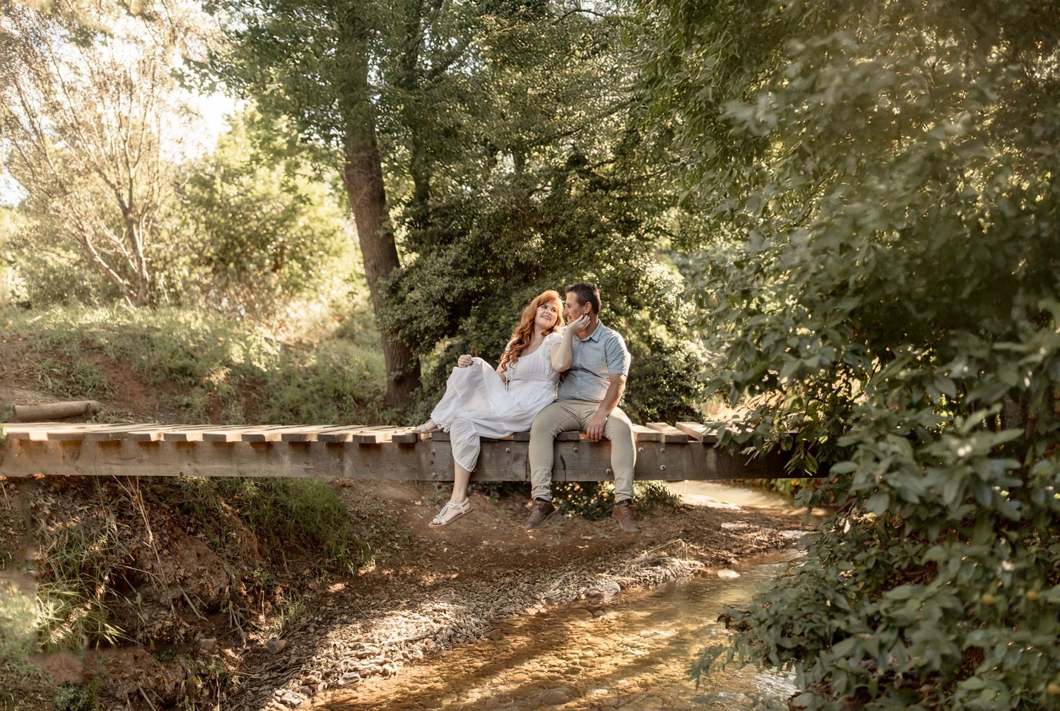 A couple sits together on a wooden bench in a serene outdoor garden setting during golden hour.