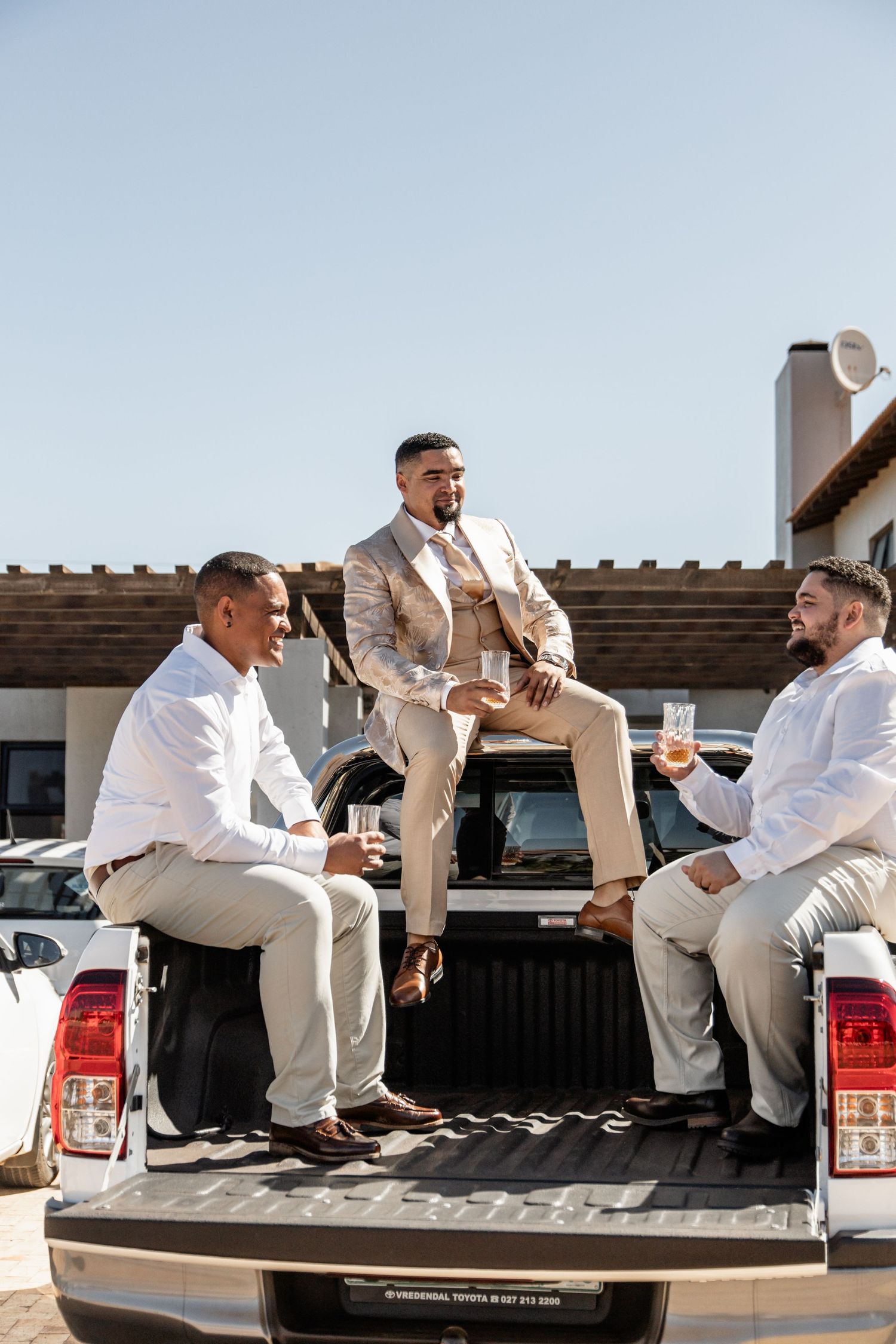 Friends hanging out and drinking beverages together in back of pickup truck on sunny day.