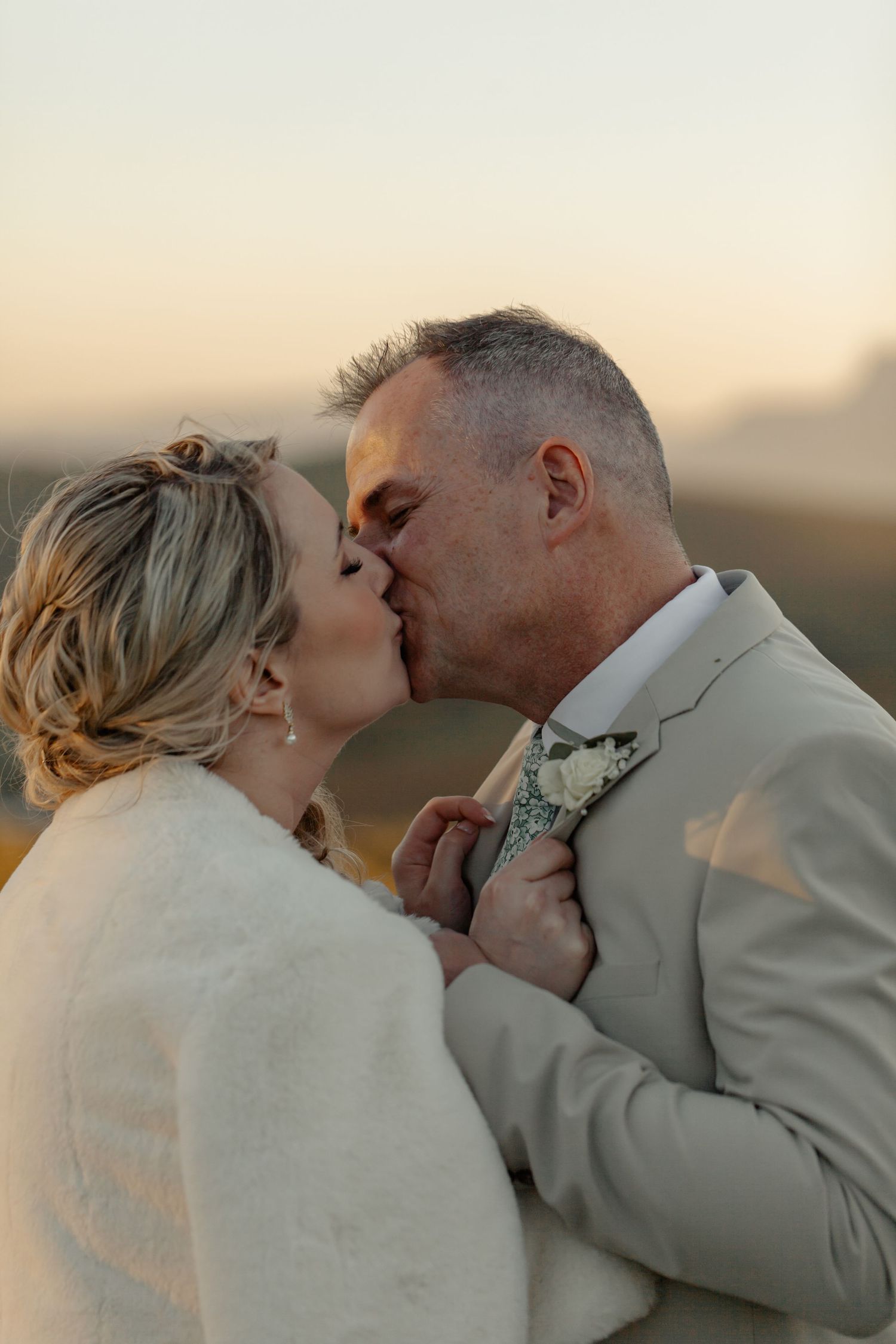 A romantic couple wearing light-colored clothing share intimate kisses in a series of outdoor sunset photos.