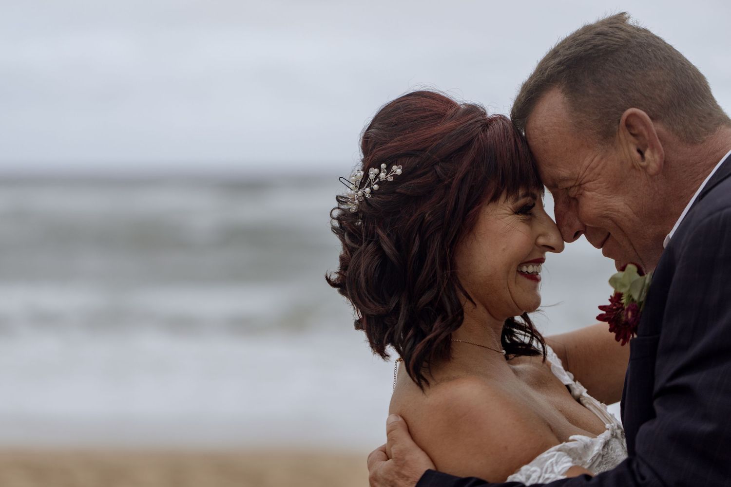 A romantic moment shared between a couple on a cloudy beach during their wedding celebration.