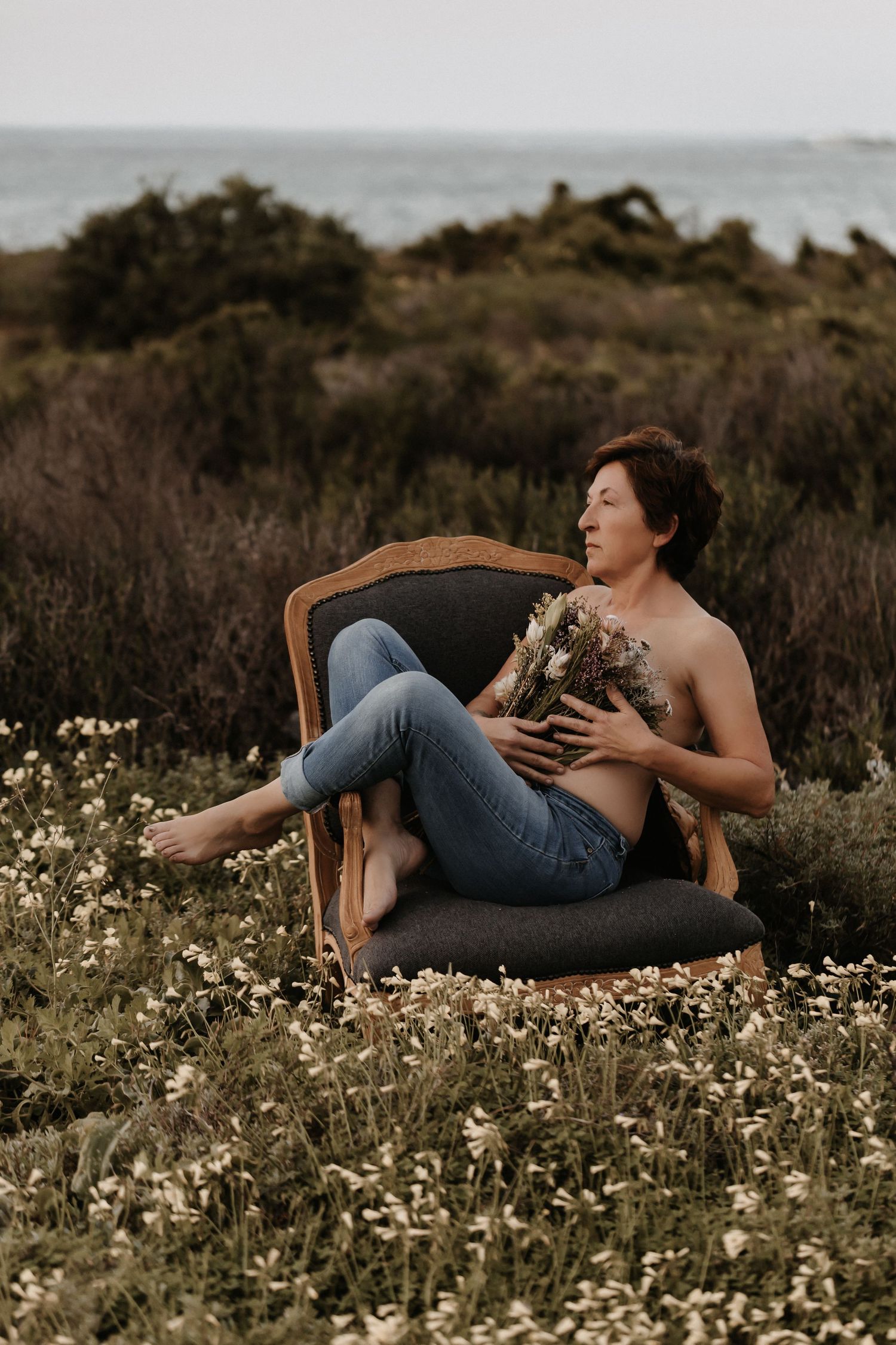 A person in denim reclines on a vintage chair amid a field of wildflowers at sunset, creating a dreamy outdoor scene.