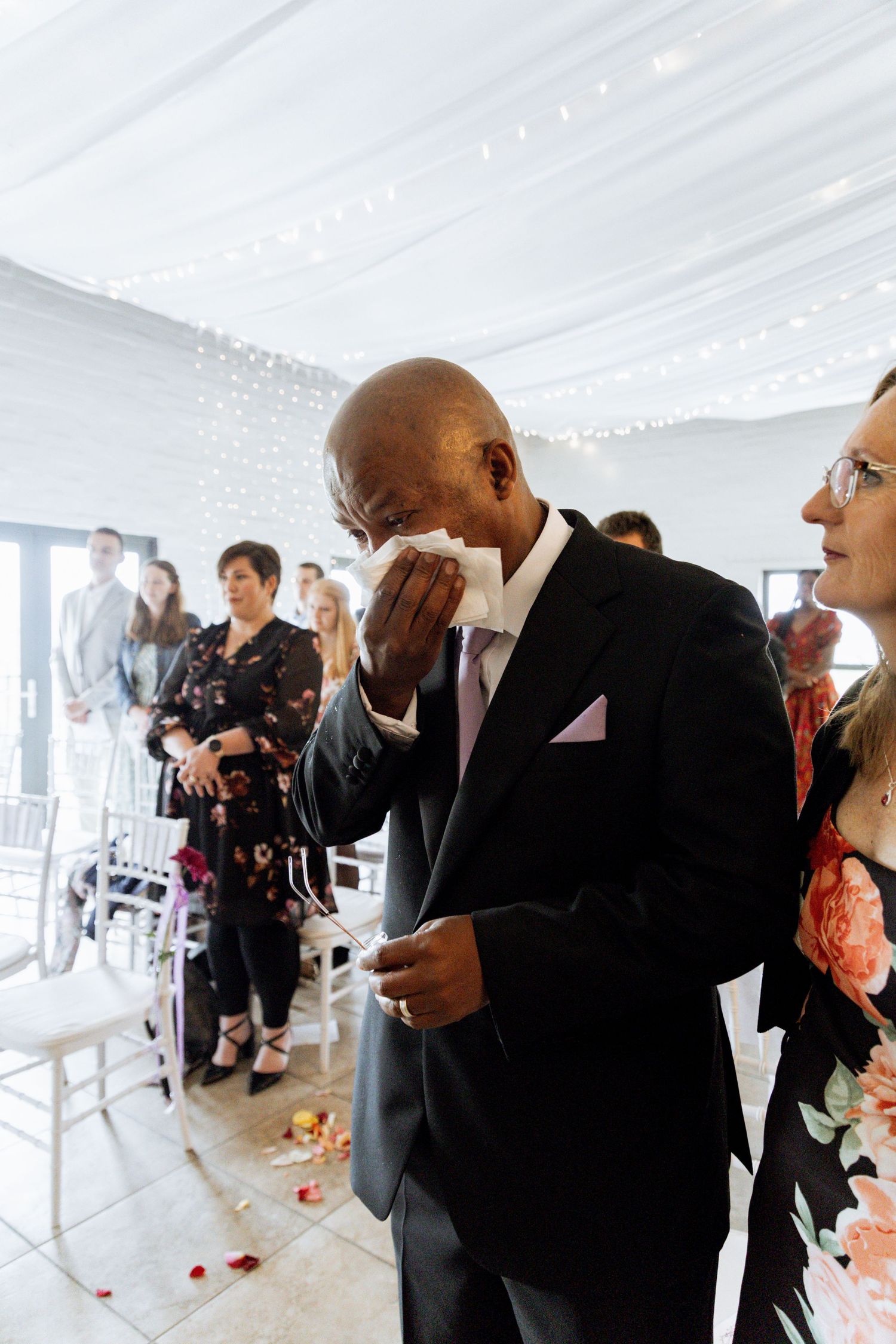 Elegantly dressed guests in formal black attire gather under a white tent during a special celebration.