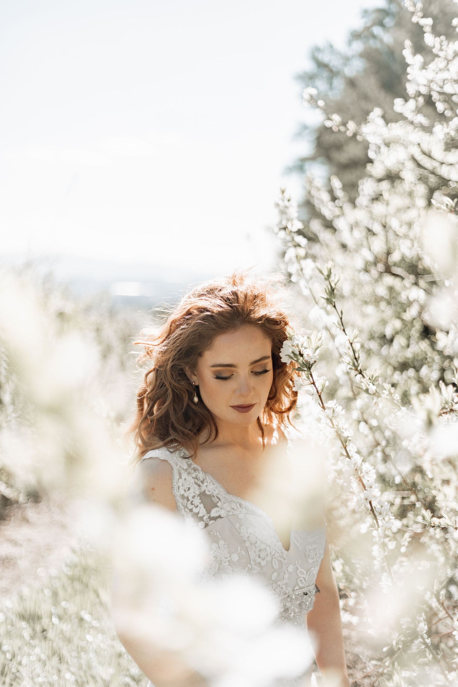 Ethereal spring portrait of woman surrounded by delicate white cherry blossoms in soft sunlight.