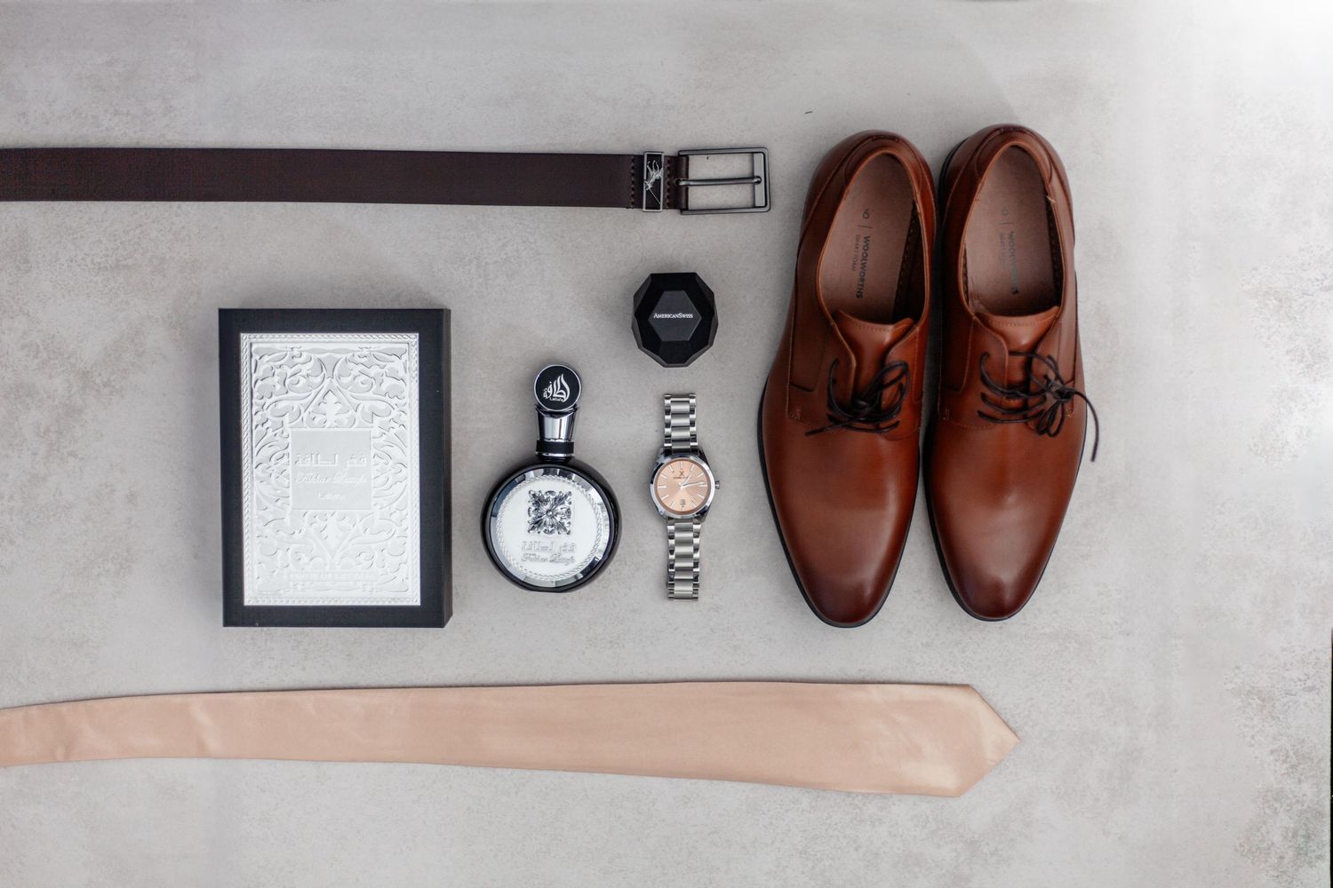 Brown leather dress shoes arranged with watches, belt, and photo frame on gray background in flat lay composition.