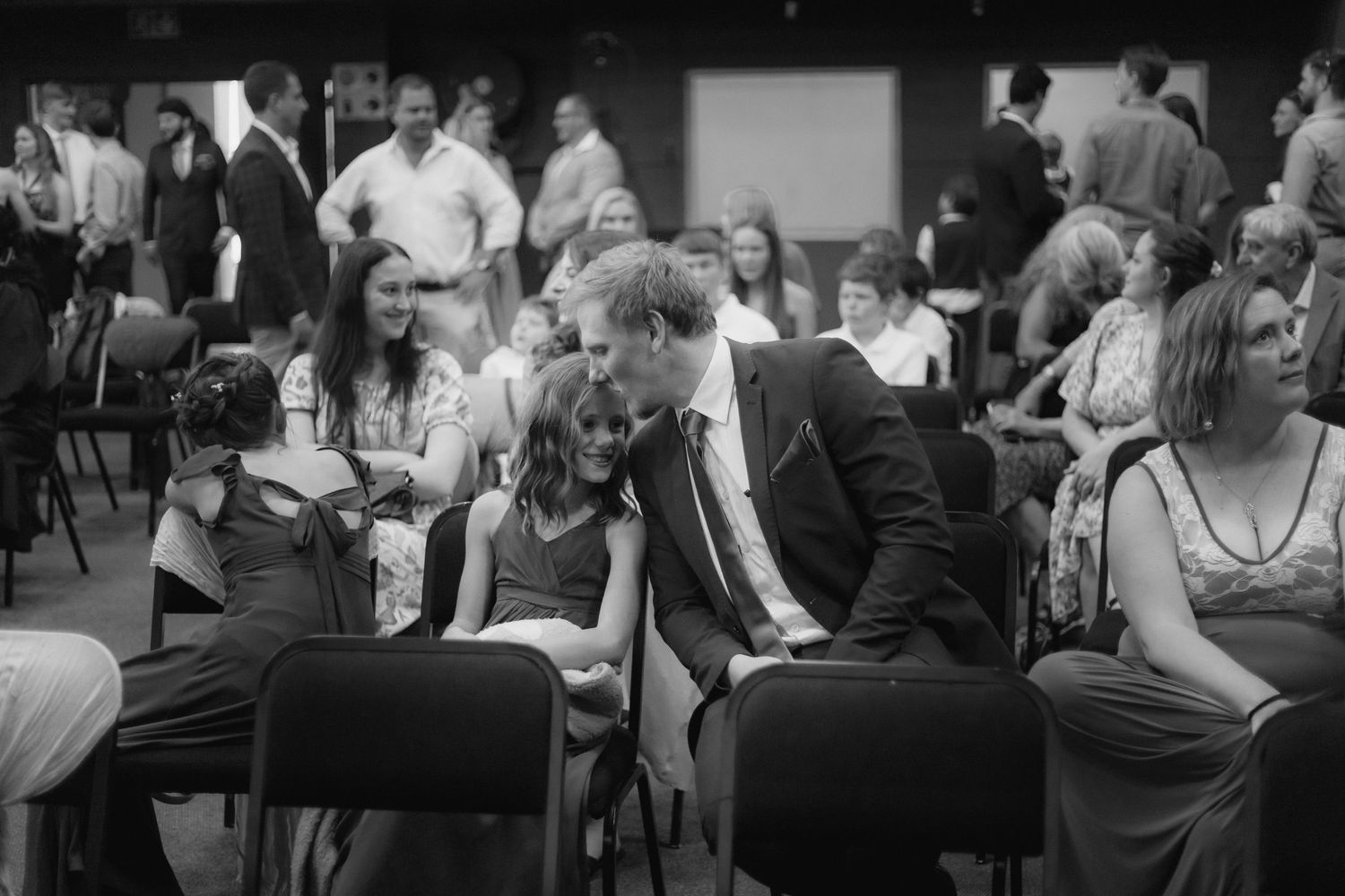 A black and white photograph of people seated in chairs at a formal event or gathering.