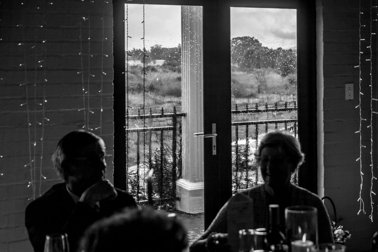 Monochrome silhouettes through a glass wall at a social establishment or venue with evening lighting.