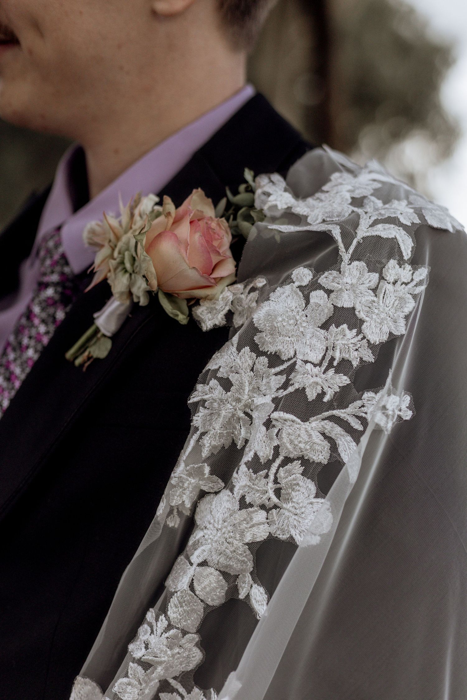 Delicate white lace floral appliques adorn the collar of a gray formal suit jacket, creating elegant wedding attire details.