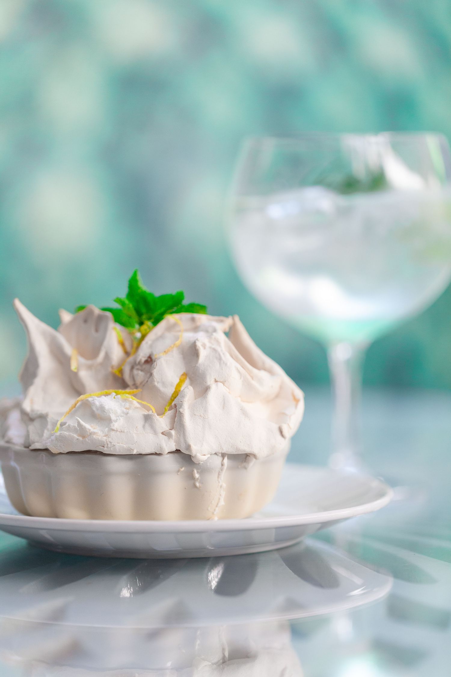 Elegant pavlova meringue desserts with mint garnish displayed on white plates against a soft turquoise background.